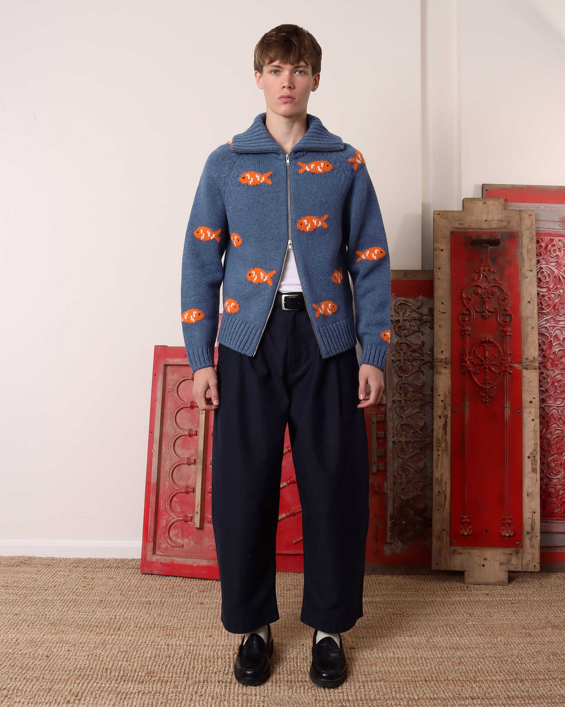 A model wears the blue 'Archie' Knit with the top half of the double zip zipped up to the collar, with the ribbed collar folded down.