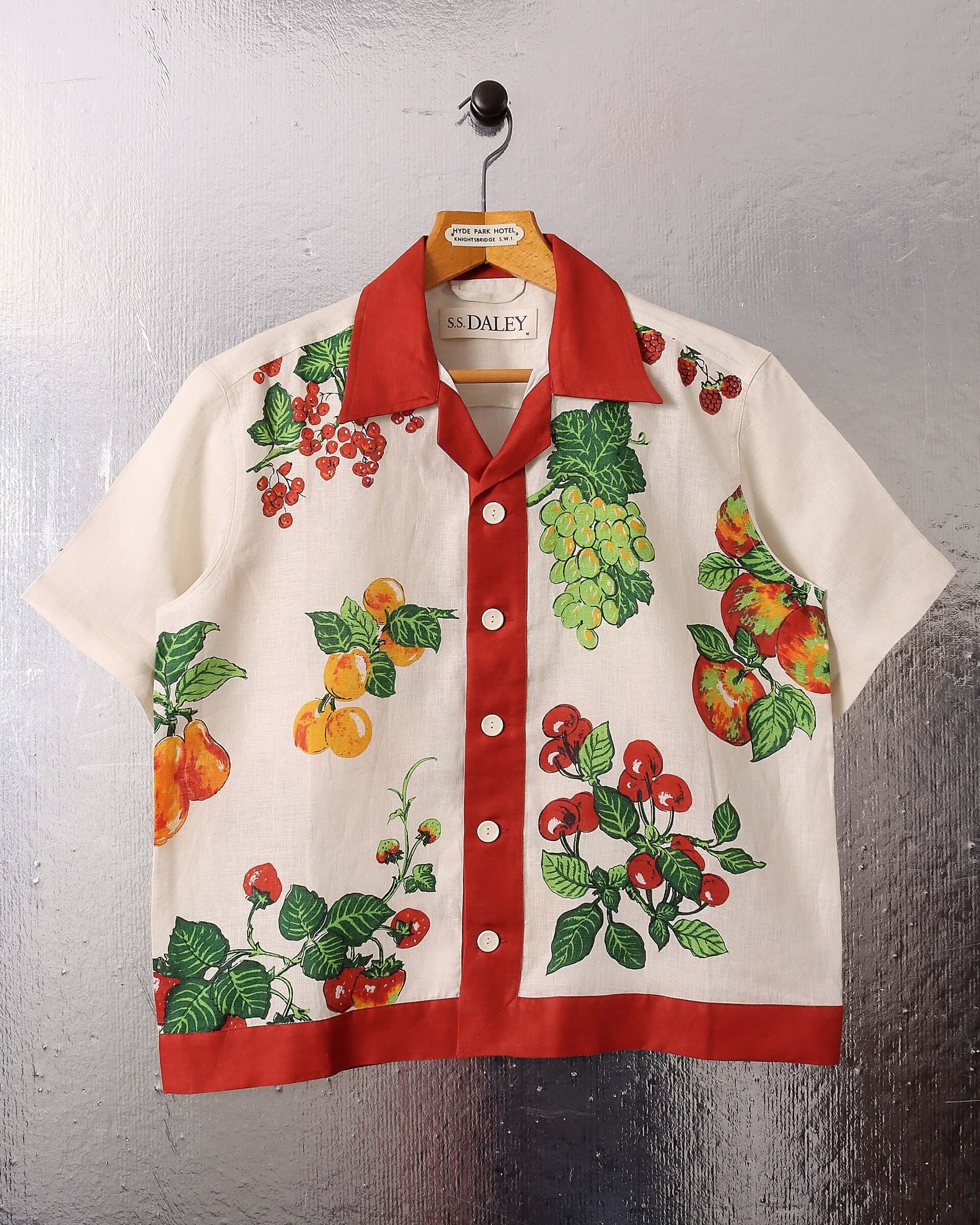 A flat shot of the 'Picnic' Shirt, showing the Irish Tea-Towel inspired colourful fruit print, and boxy, vibrant red lining along the front placket, hem, and camp collar.