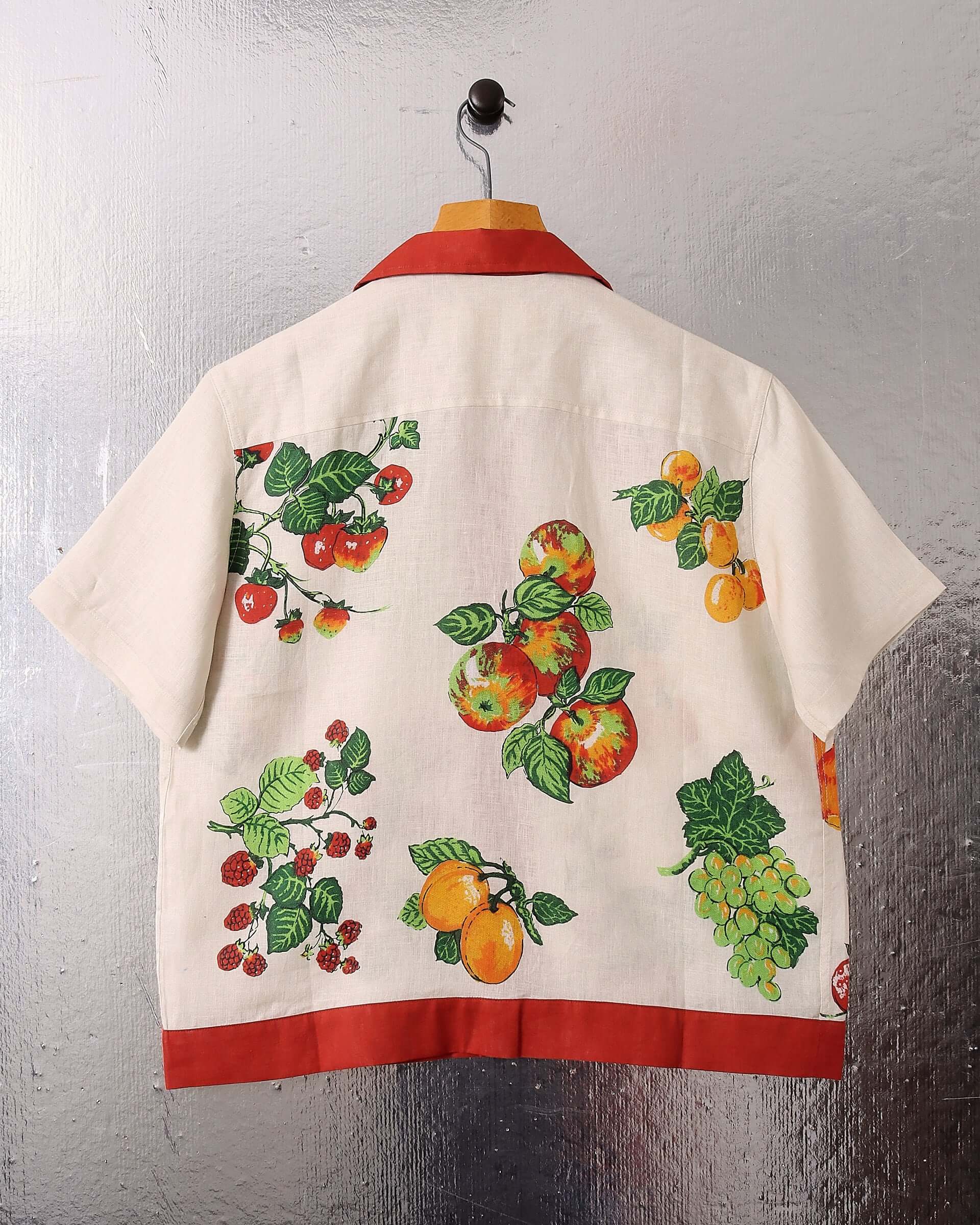 A flat shot of the short sleeve 'Picnic' Shirt  showing the back fruit print and red lining on the hem and collar.