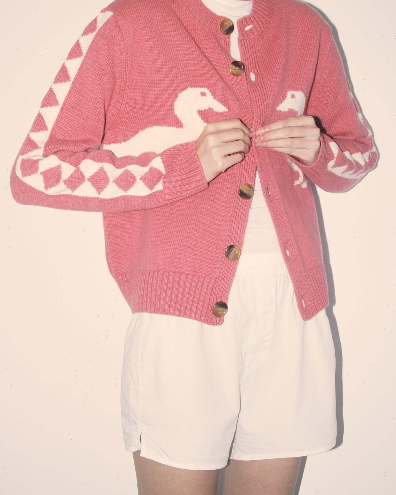 A detail shot of the 'Jasper' Cardigan in pink with two white duck motifs, white geometric motifs down the sleeves, and six brown buttons.