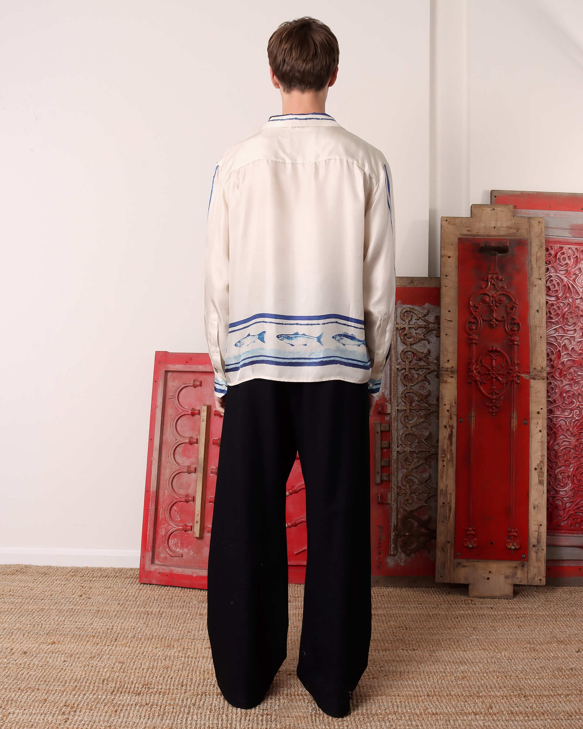 A model shows the back of the 'Elliot' Silk Shirt and the continuation of the blue fish print that goes along the back bottom.