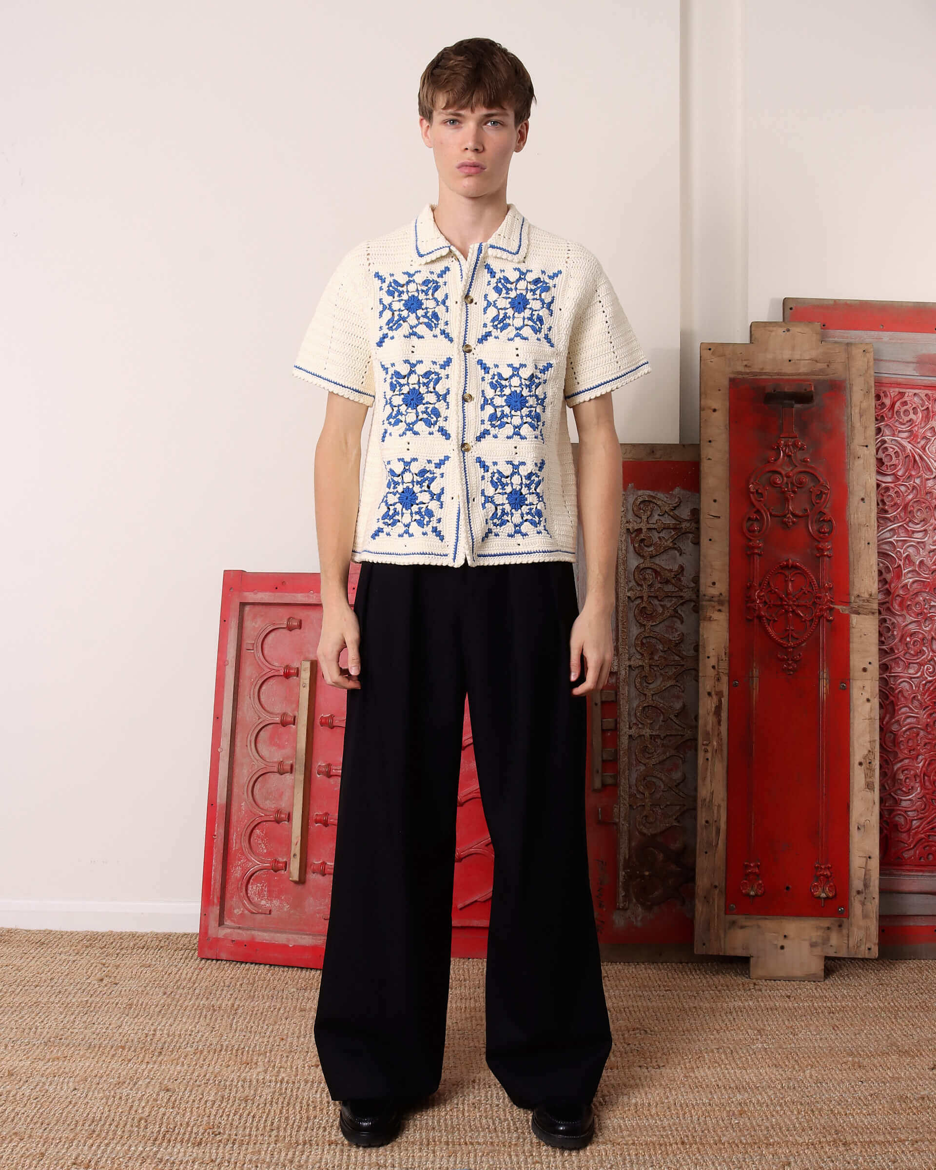 A model wears the 'Abel' Crochet Shirt in cream and blue with a pair of black 'George' Trousers.