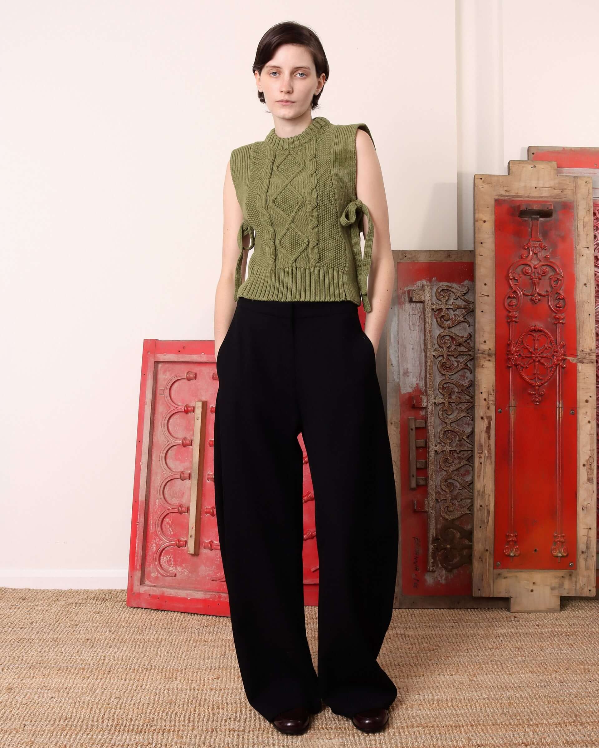 A model wears the green 'Blandine' Vest with the side-ties tied in a bow, paired with black trousers.