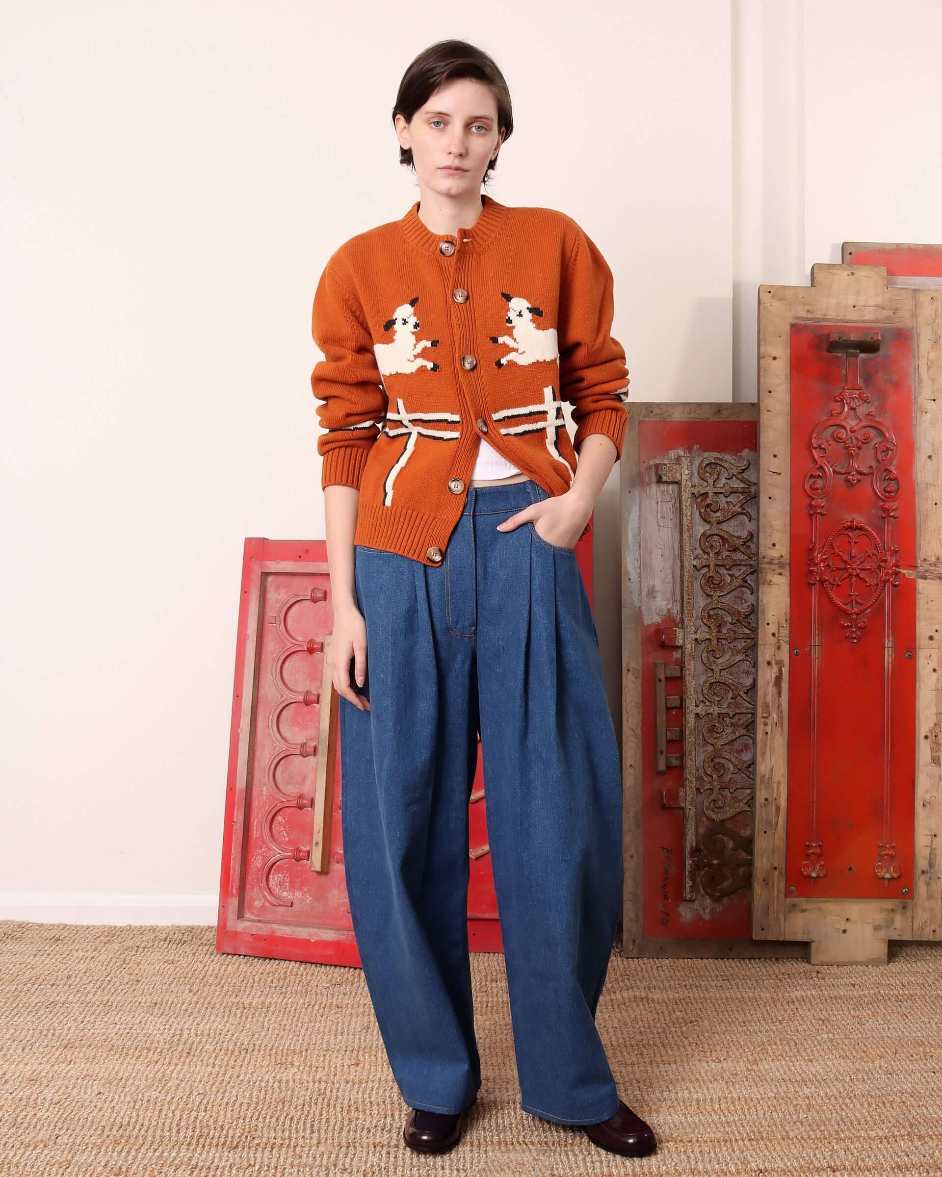 A model wears the 'Cyril' Lamb Cardigan in Tawny, a burnt orange colour.