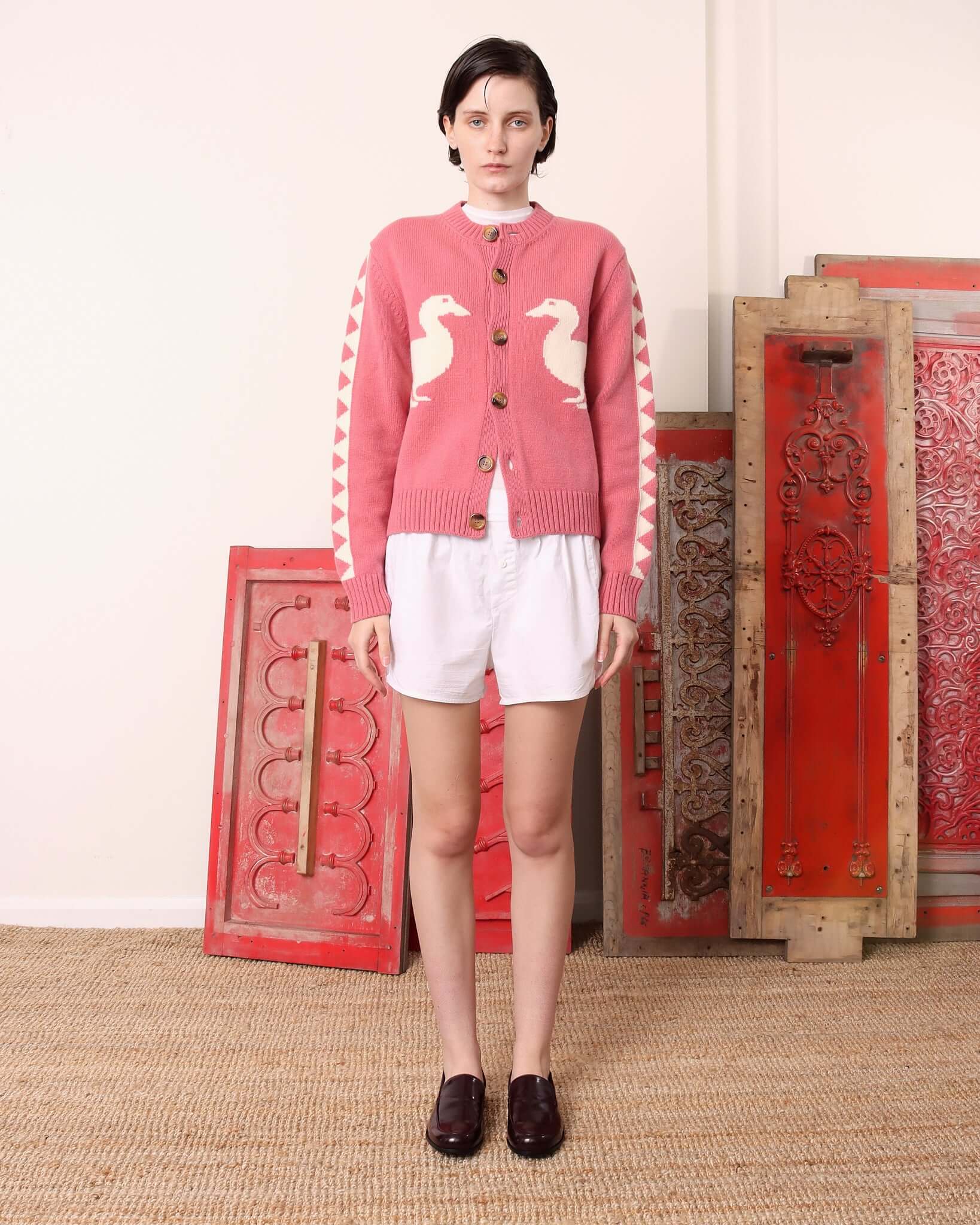 A model wears the 'Jasper' Cardigan in pink with white shorts.