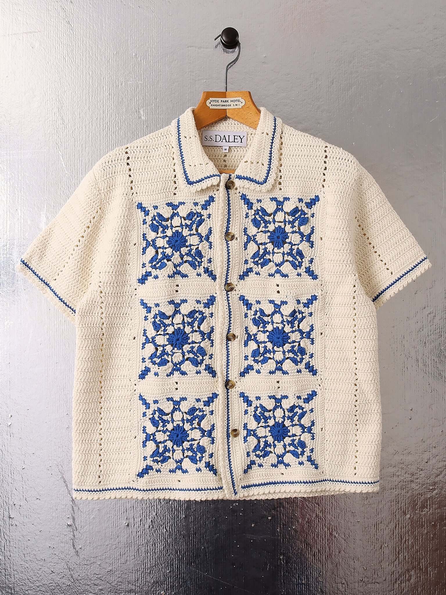 A flat shot of the 'Abel' Crochet Shirt in blue on a hanger showing the geometric crochet details.