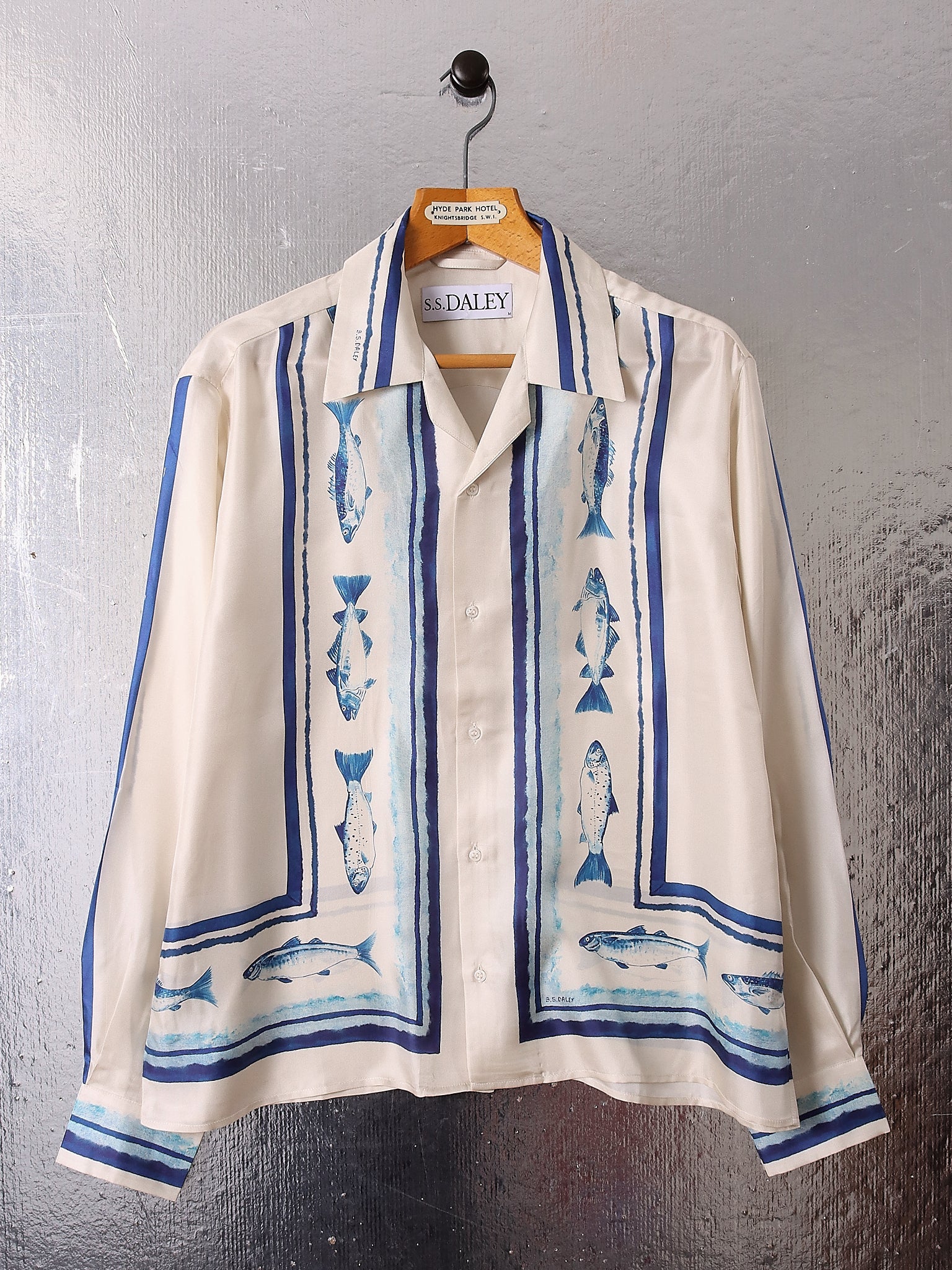 A flat image of the 'Elliot' Silk Shirt on a hanger showing the fish print in a mixture of electric and muted blue tones on a silk ecru base.