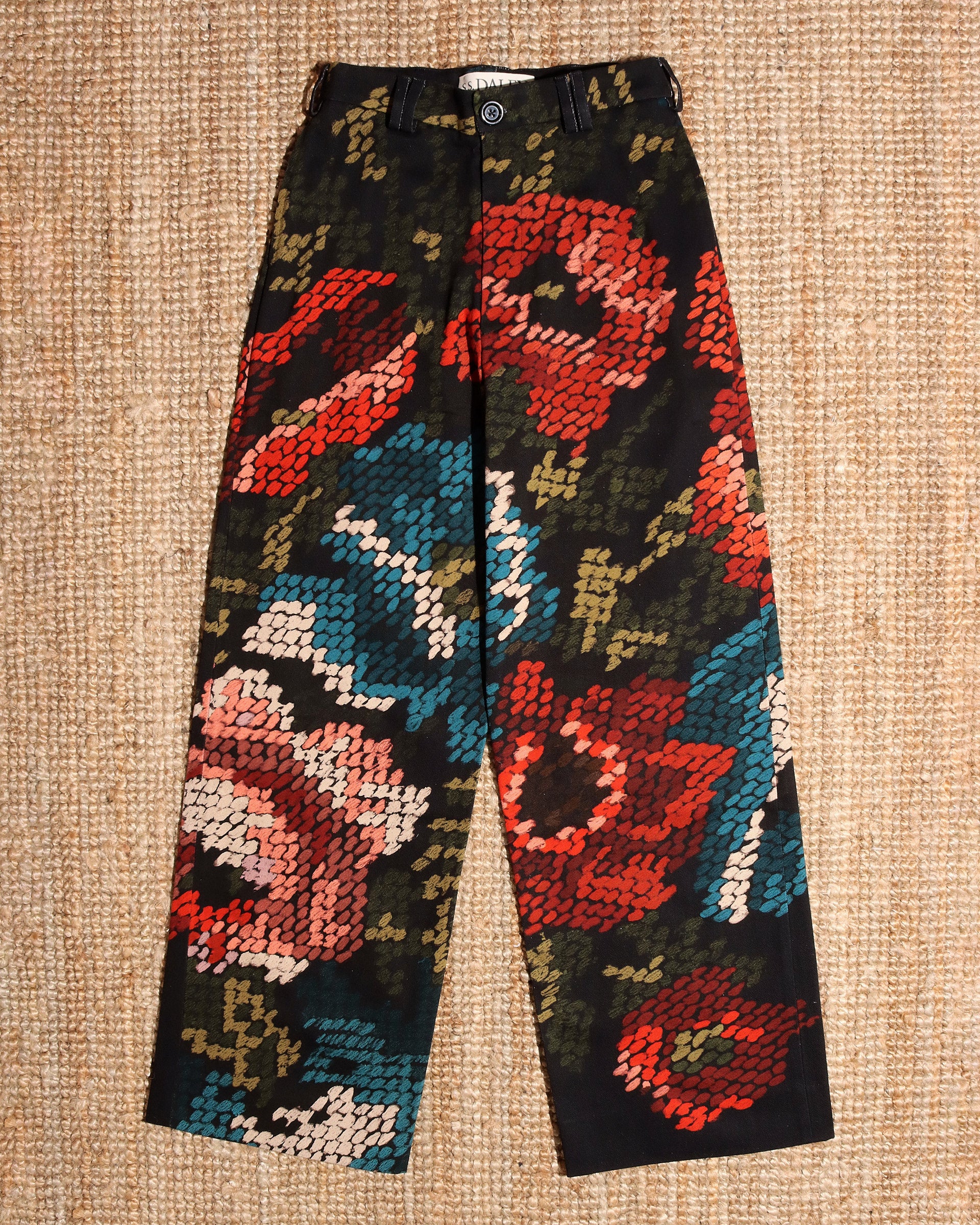 A flat sht of the 'Spry' Trousers which have colourful blue, red, and green flower prints on a black  base.