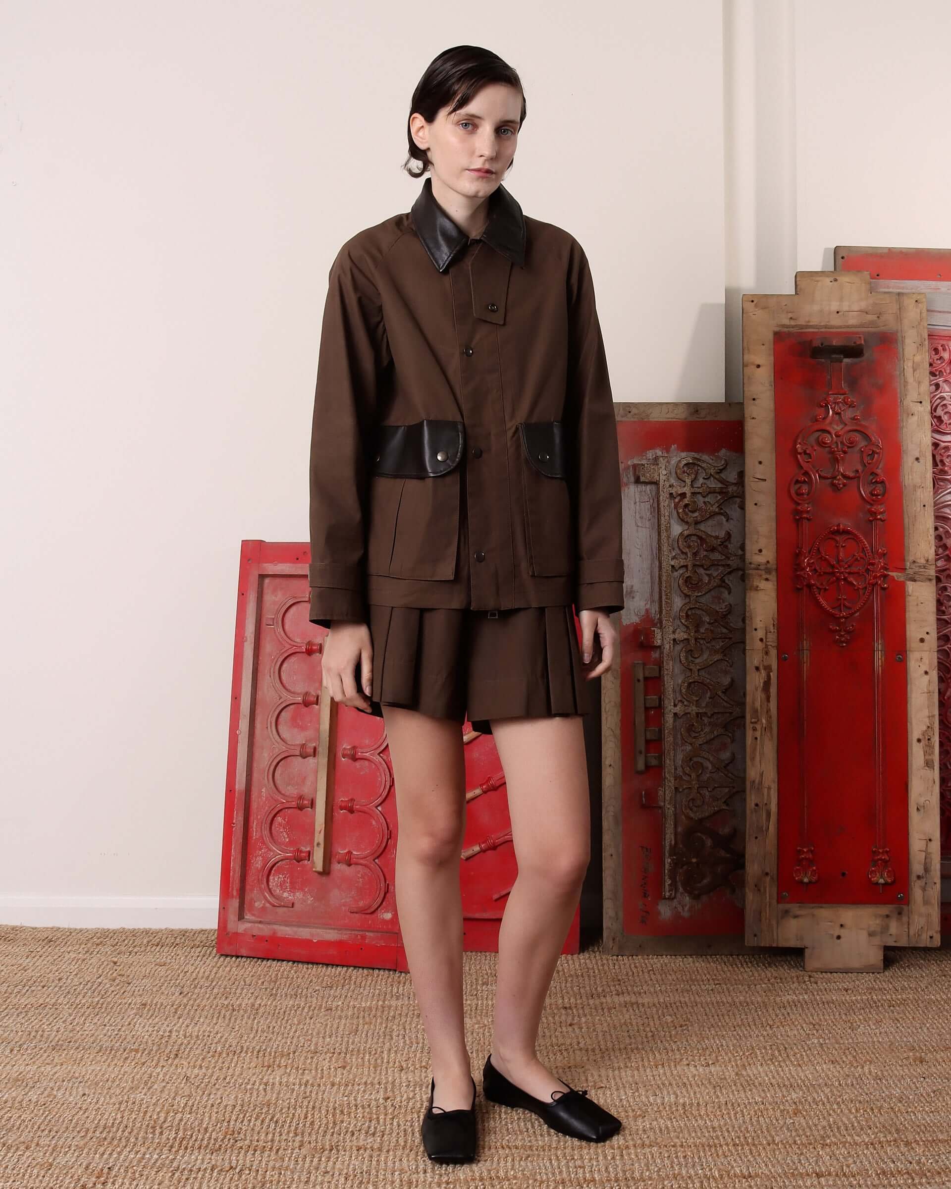 A model wears the 'Thea' Waxed Blouson Jacket with matching dark brown pleated shorts.