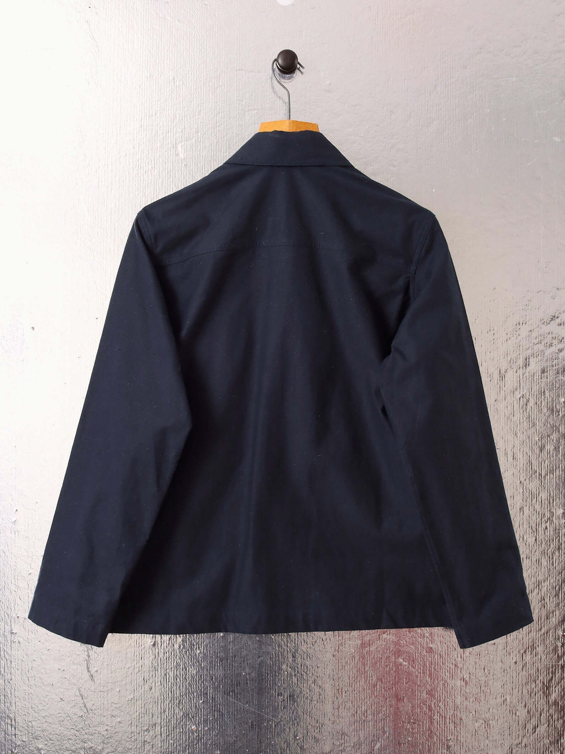 A flat shot of the back of the 'Clarence' Chore Jacket in navy on a hanger.