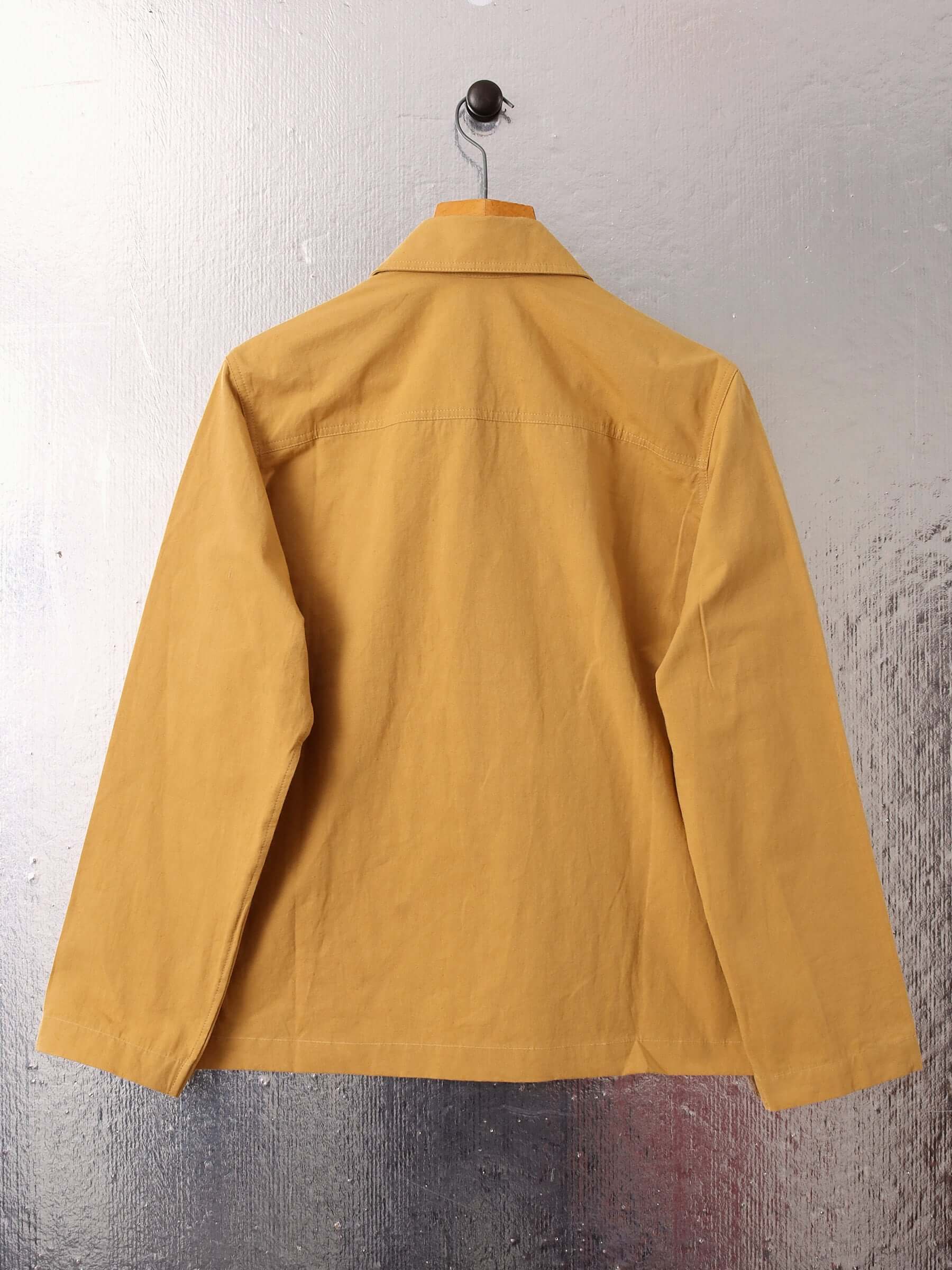 A flat shot of the back of the 'Clarence' Chore Jacket in mustard, showing the shape of the garment.
