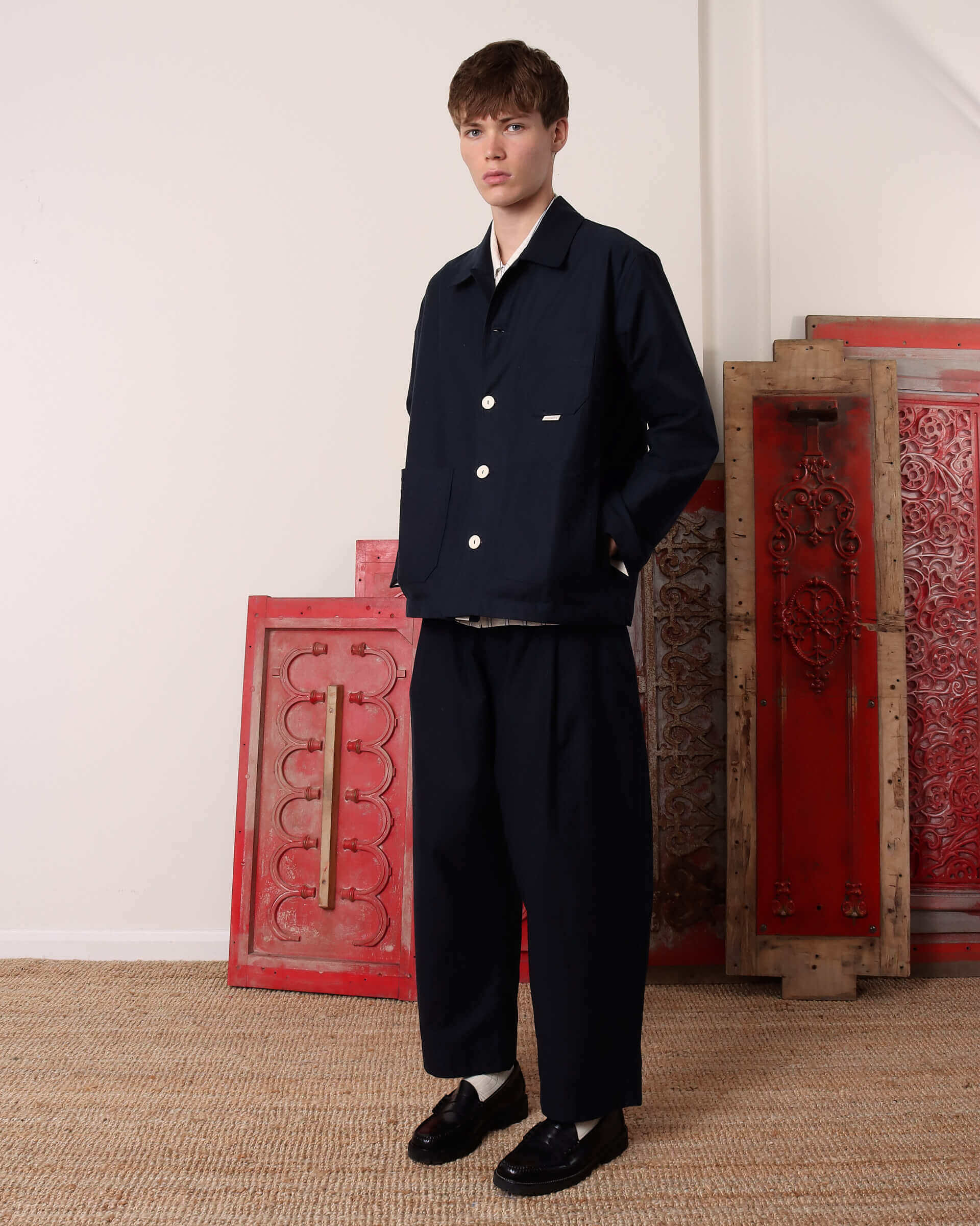 A model shows the side of the 'Clarence' Chore Jacket in navy, with three buttons done and his hands in the two front pockets.
