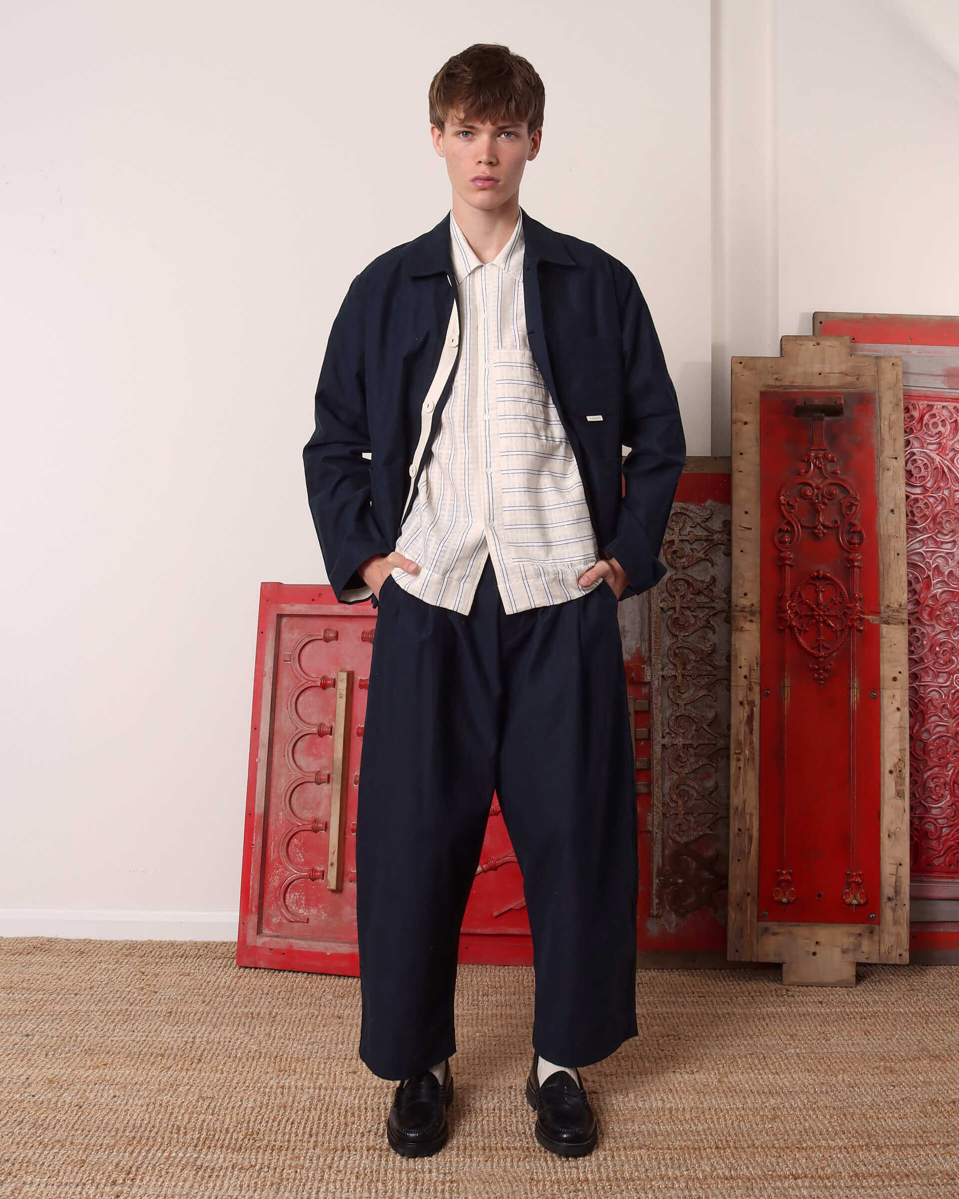 A model wearing the 'Clarence' Chore Jacket in navy open with his hands in the pockets of the matching 'Clarence' Trousers.