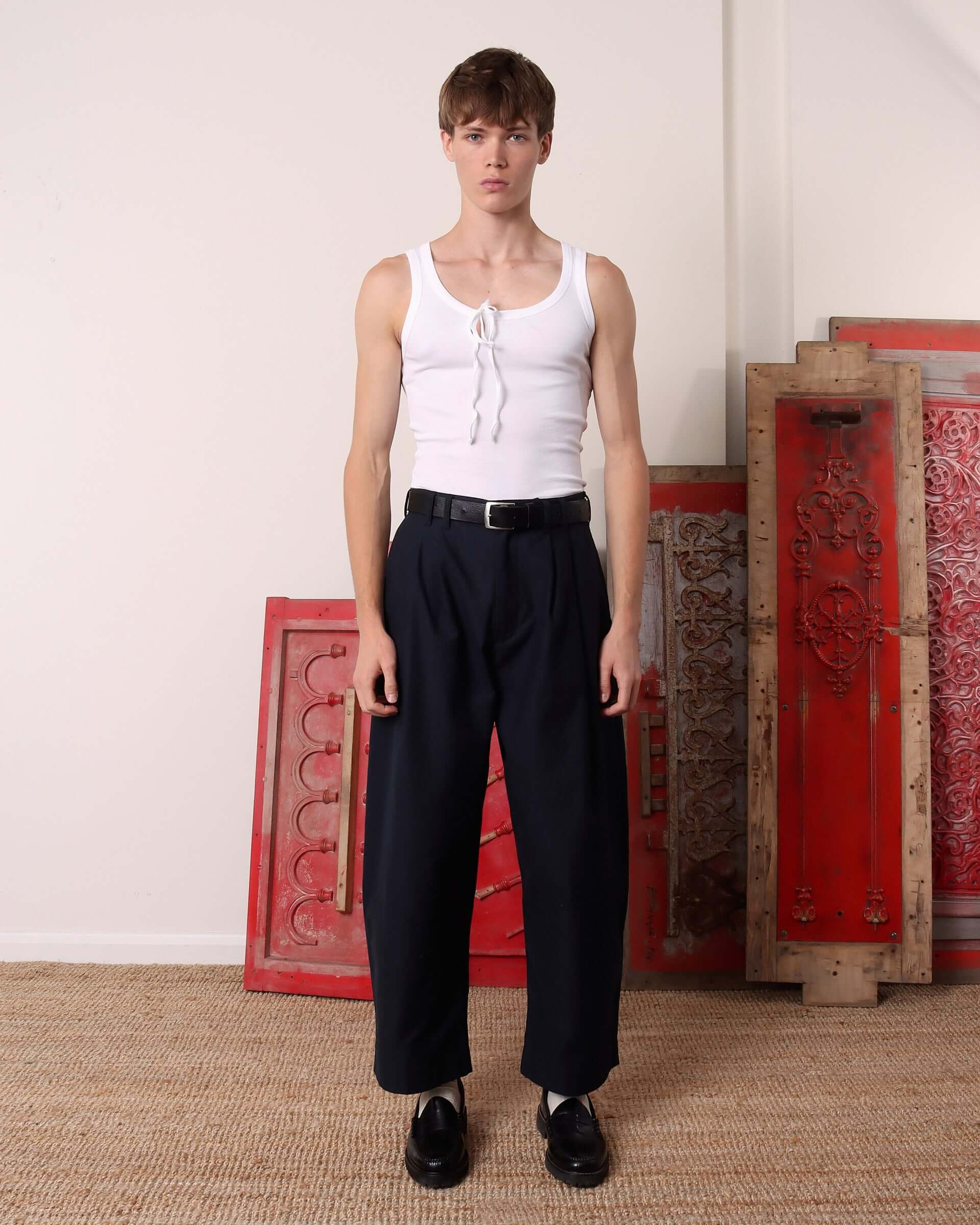 A model wears the 'Cochrane' vest in white tucked into the double pleated 'Clarence' Trousers in navy. 