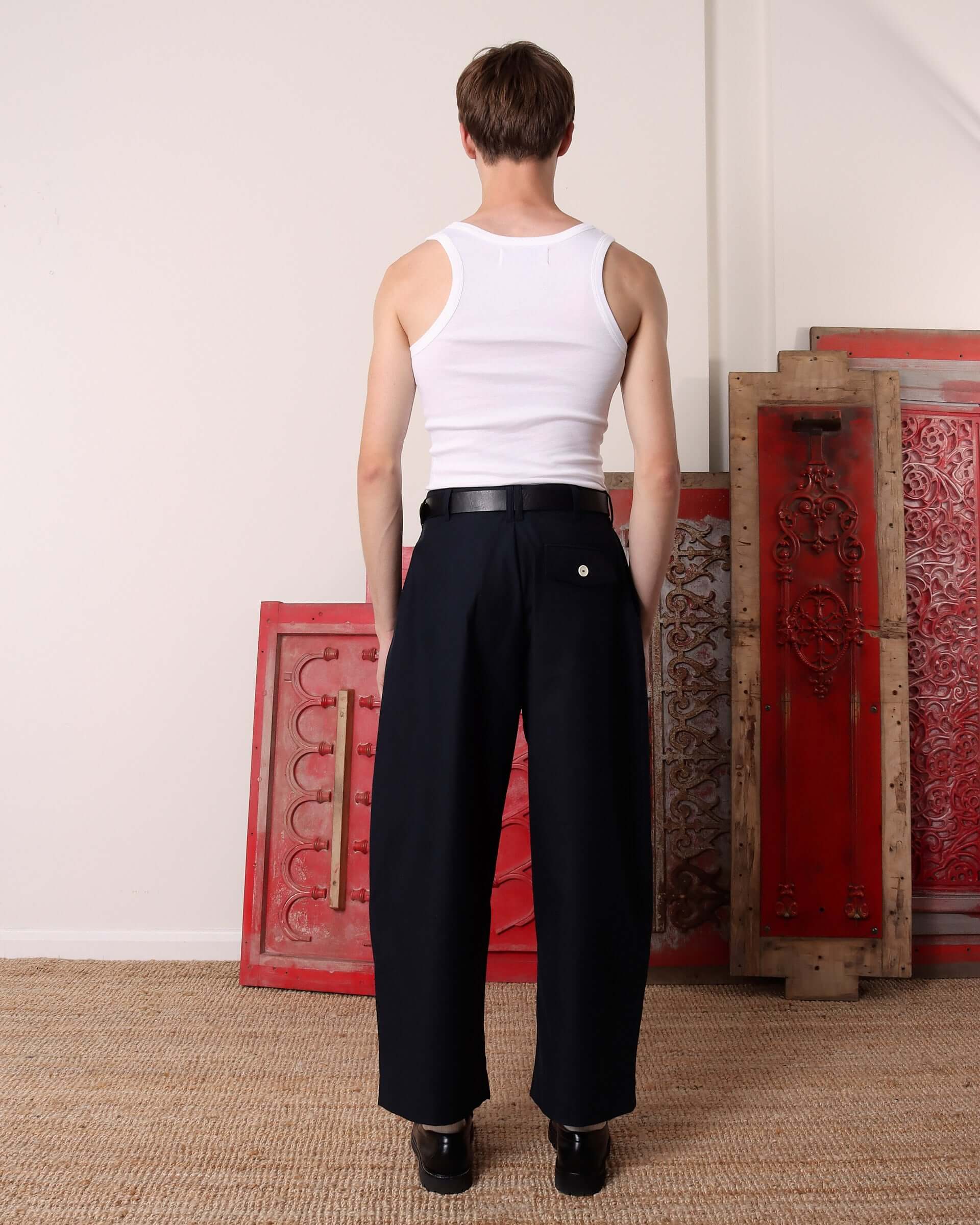 A model shows the back of the 'Clarence' Trousers in navy, showing the back pocket with a white button closure.