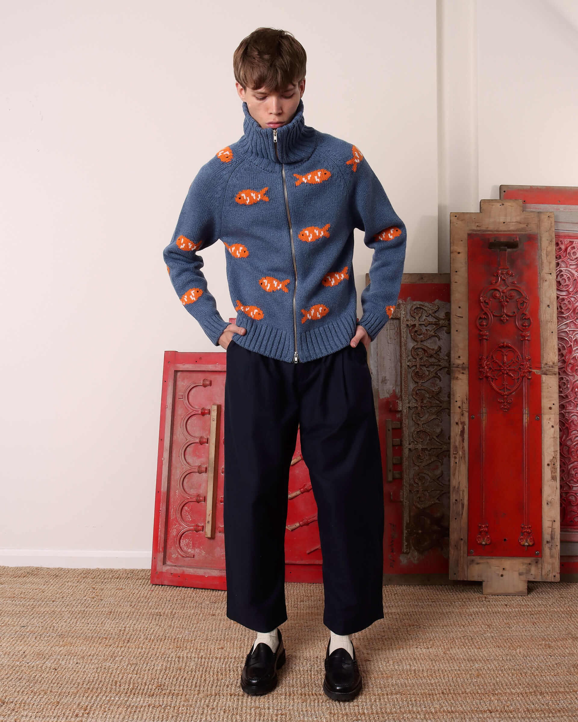 A model wears the 'Archie' Knit with the double zip zipped all the way up, creating a high neck collar.
