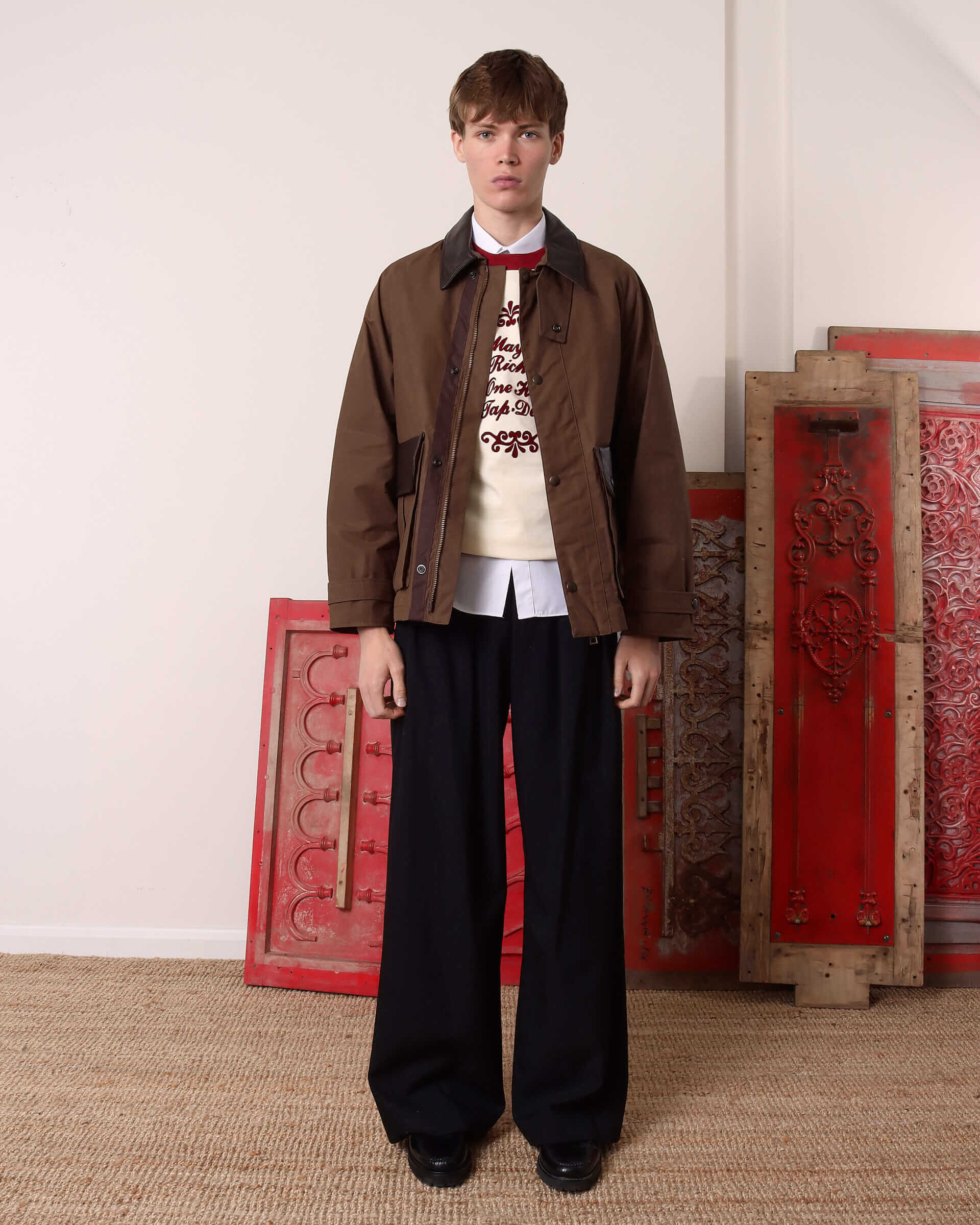 A model wears the 'Theodore' Waxed Blouson Jacket open styled with a ecru and burgundy 'Tap' T-shirt over a button-up shirt with a pair of black trousers.