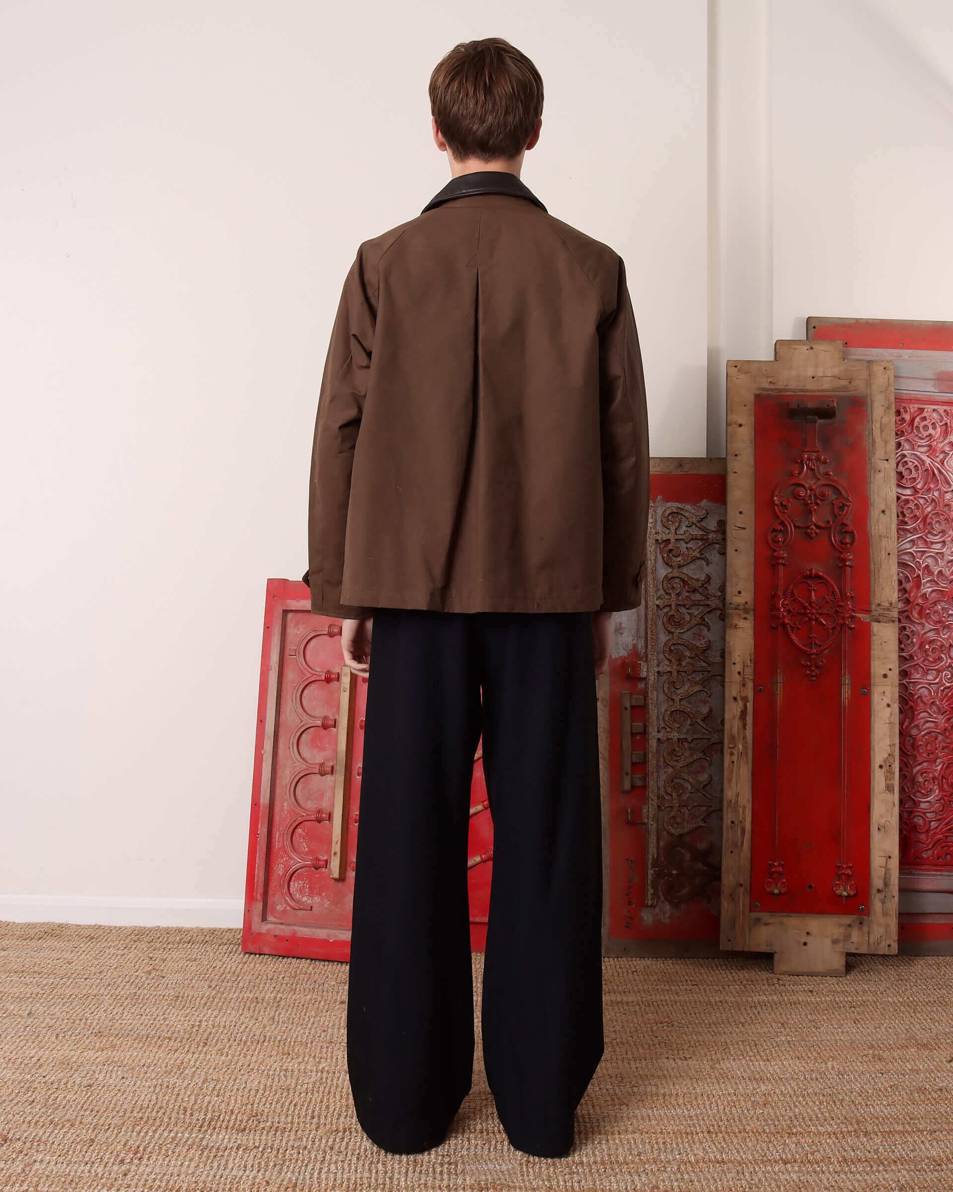 A model shows the back of the 'Theodore' Wax Blouson Jacket and its back pleated detail.