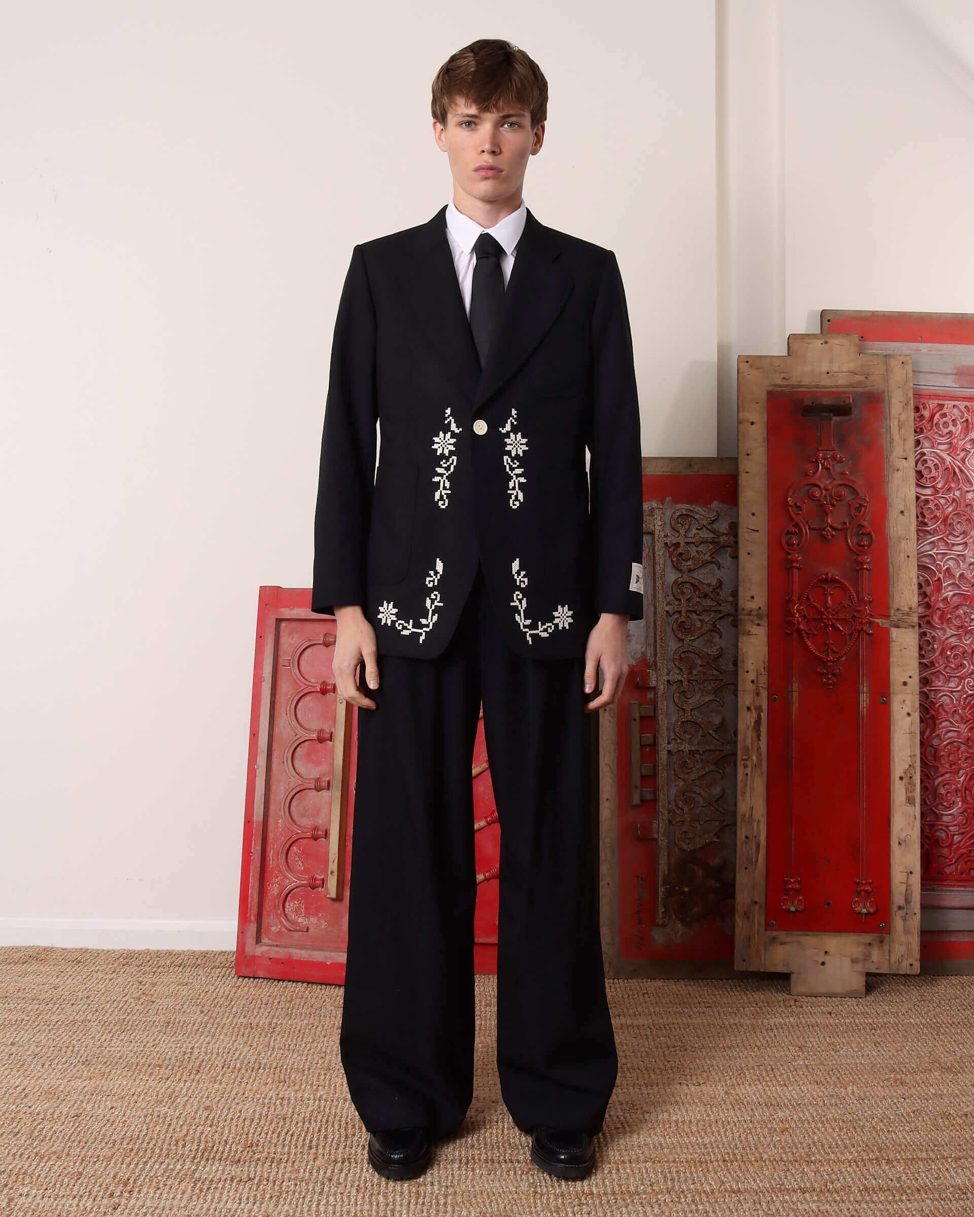 A model wears the 'Albert' Single-Breasted Suit Jacket buttoned with a shirt and tie underneath and matching black trousers.