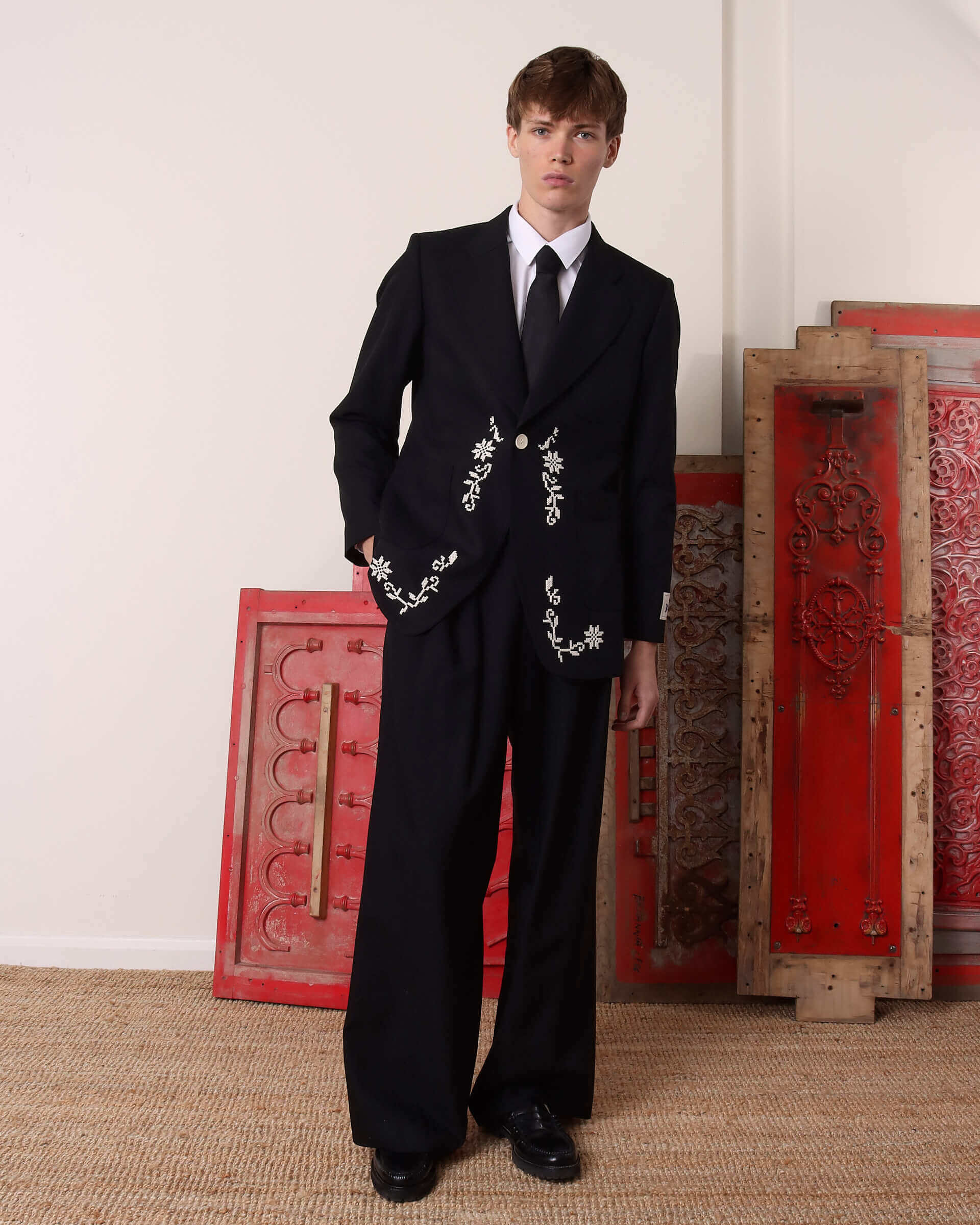A model wears the black 'Albert' Suit Jacket and matching black trousers with one hand in the pocket. 
