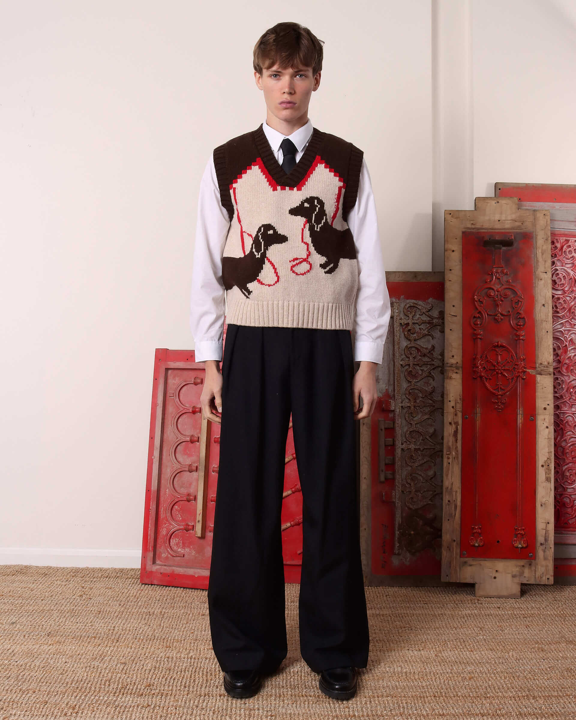 A model wears the 'Harold' Sweater Vest in brown and ecru, with a shirt and tie on underneath and a pair of black trousers.