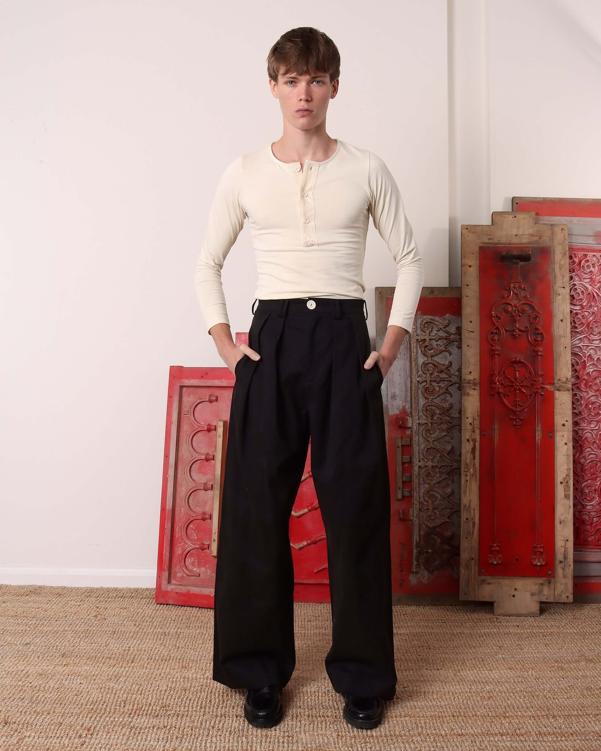 A model wears the 'Harold' Henley Shirt in Ecru tucked into a pair of 'George' Trousers. 