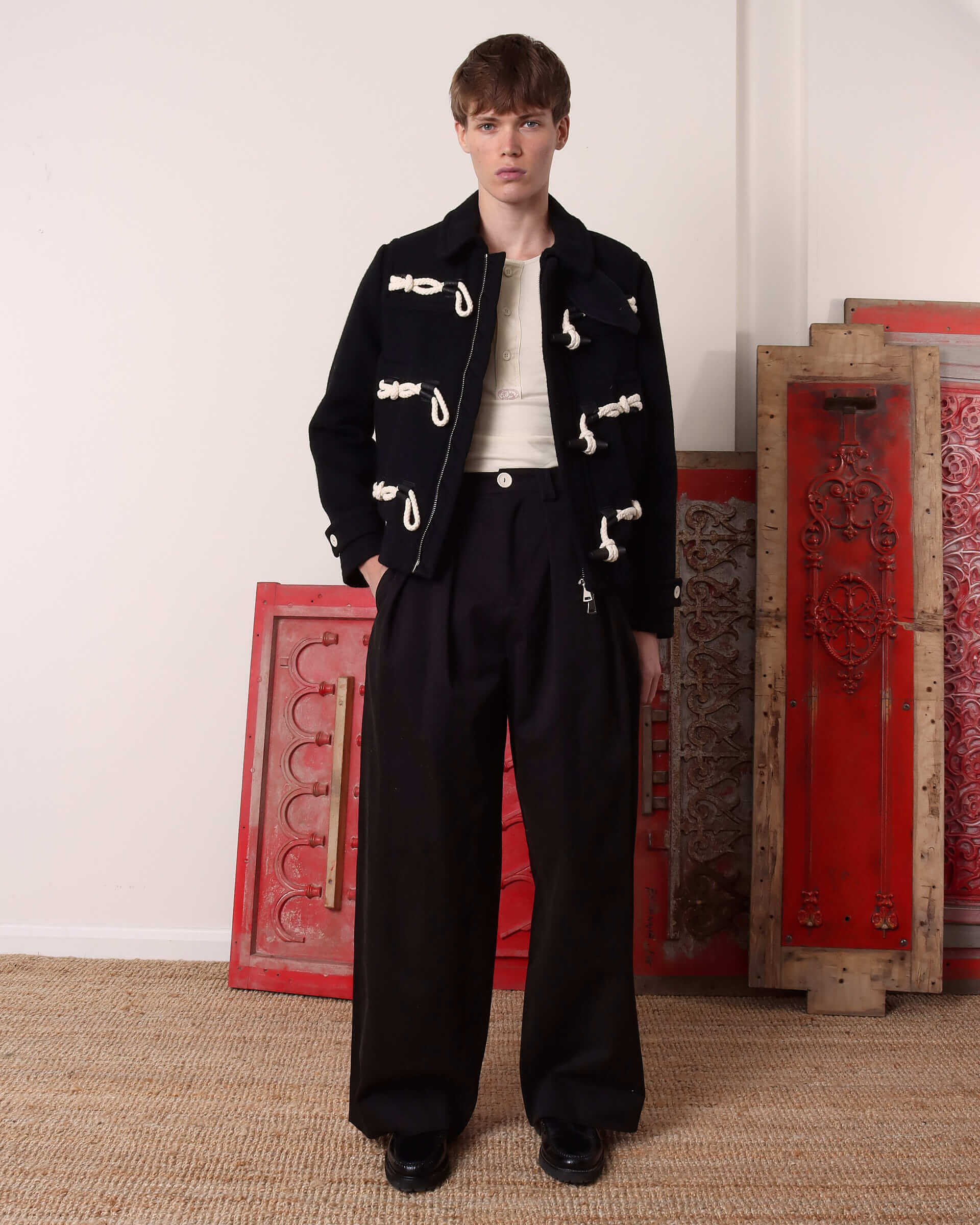 A model wears the 'Alwyn' Duffle Jacket with the zip open paired with the black 'George' Trousers. 