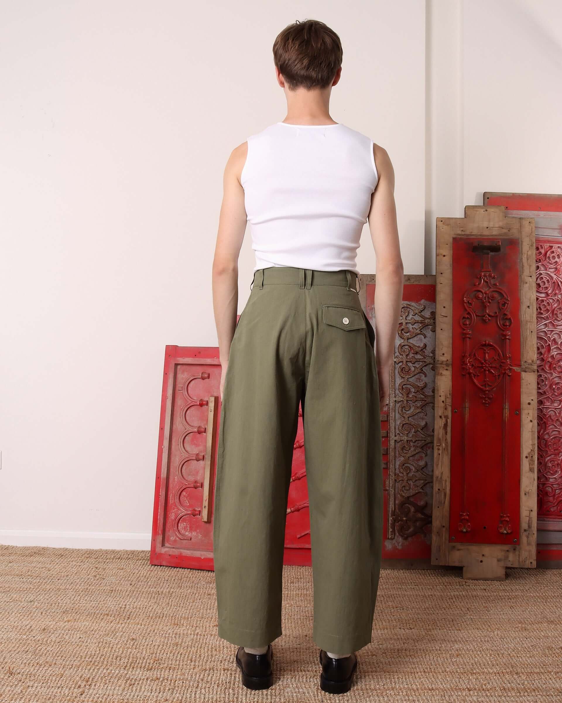 A model shows the back of the 'Clarence' Trousers in khaki green, which shows the back pocket with a white button closure.