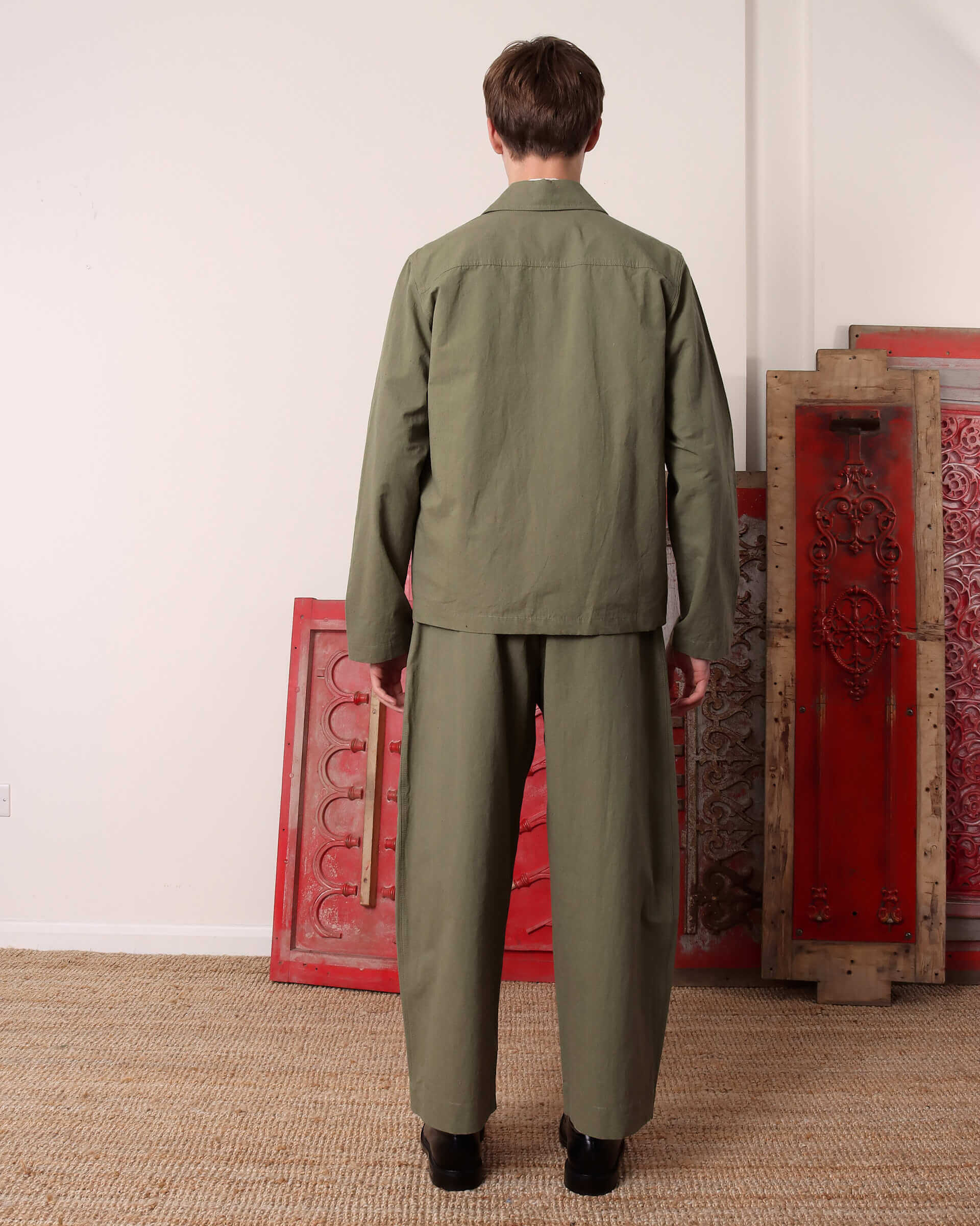 A model shows the back of the green 'Clarence' Chore Jacket and matching green 'Clarence' Trousers. 