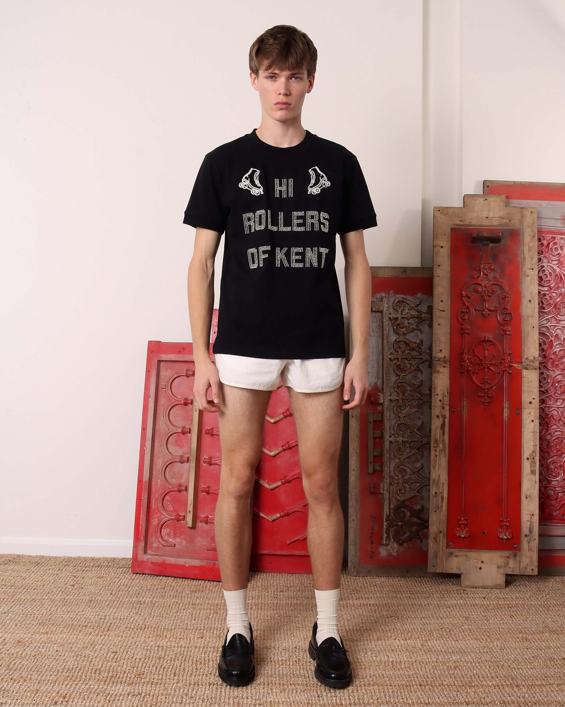 A model wears the black 'Hi Rollers' T-shirt untucked paired with white drawstring shorts.