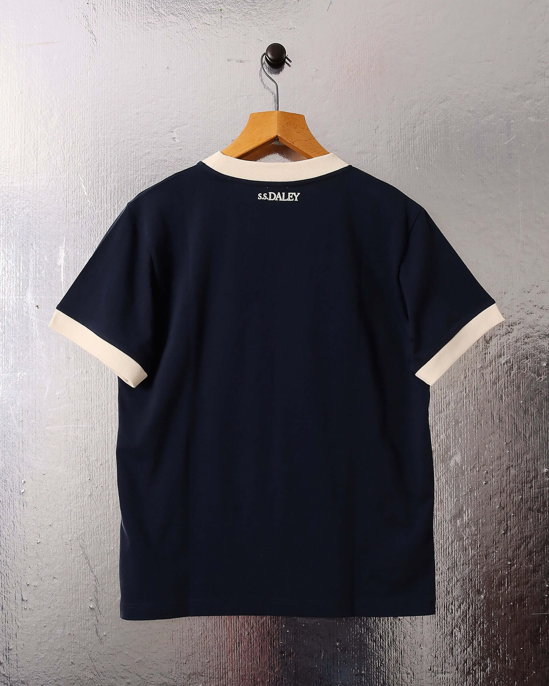 A flat image of the navy 'Tap' T-shirt on a hanger, showing the back and the intricate S.S.DALEY logo towards the top of the garment near the neckline.