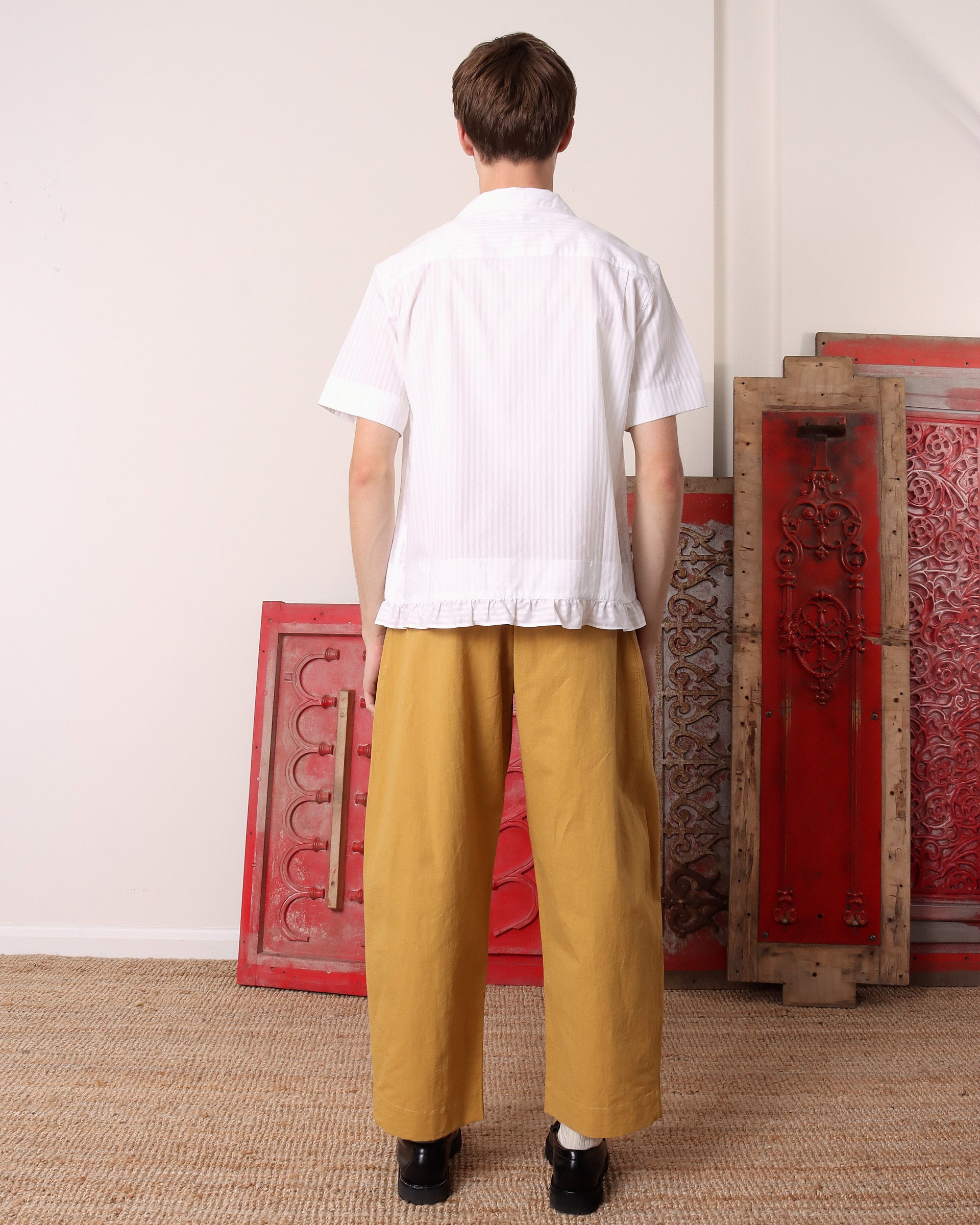 A model shows the back of the he 'Oxford' Striped Pillowcase Shirt in white stripes and the continued ruffles on the hem.