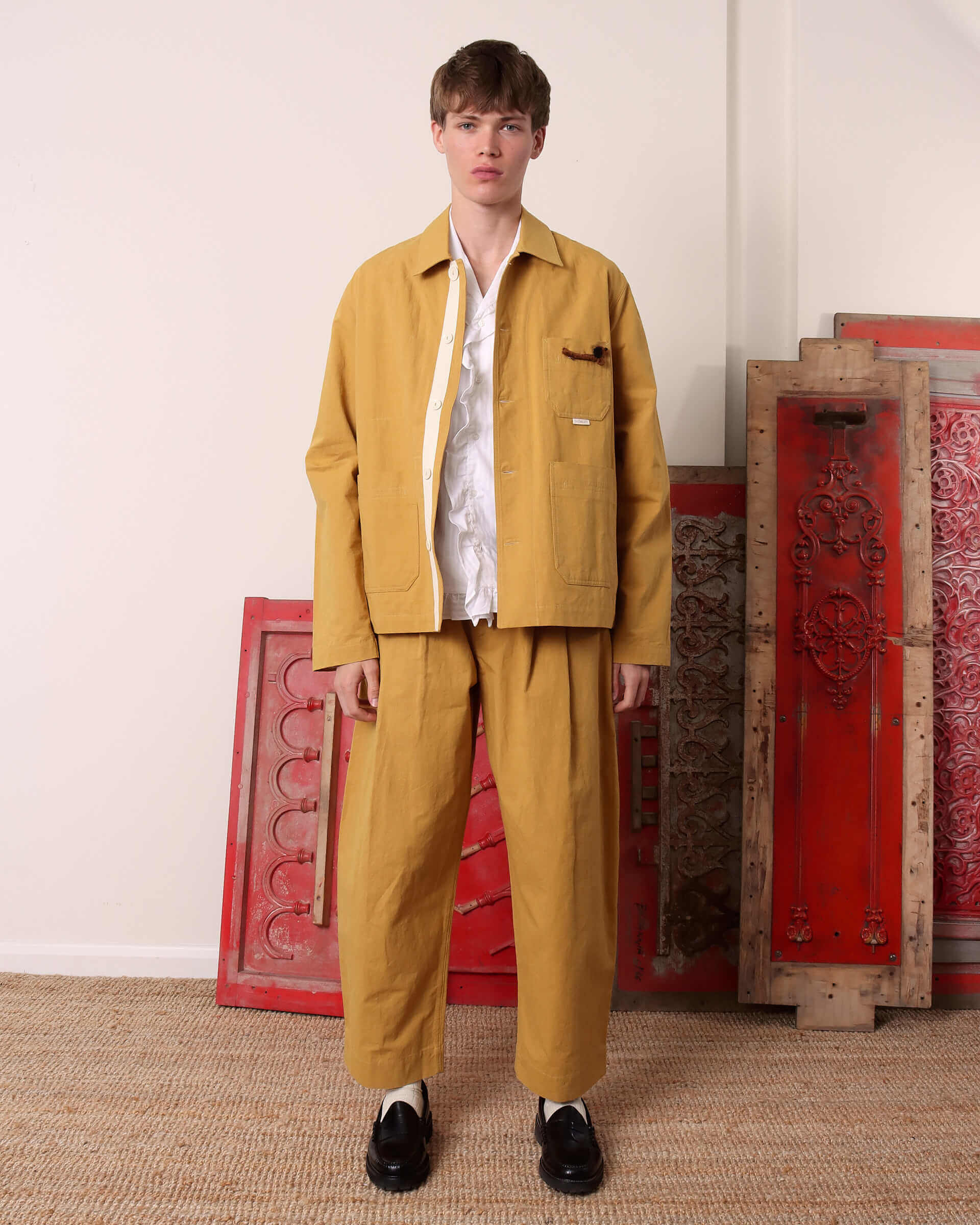 A model wears the 'Clarence' Chore Jacket in mustard open, showing the boxy style, matched with the 'Clarence' Trousers in mustard. 