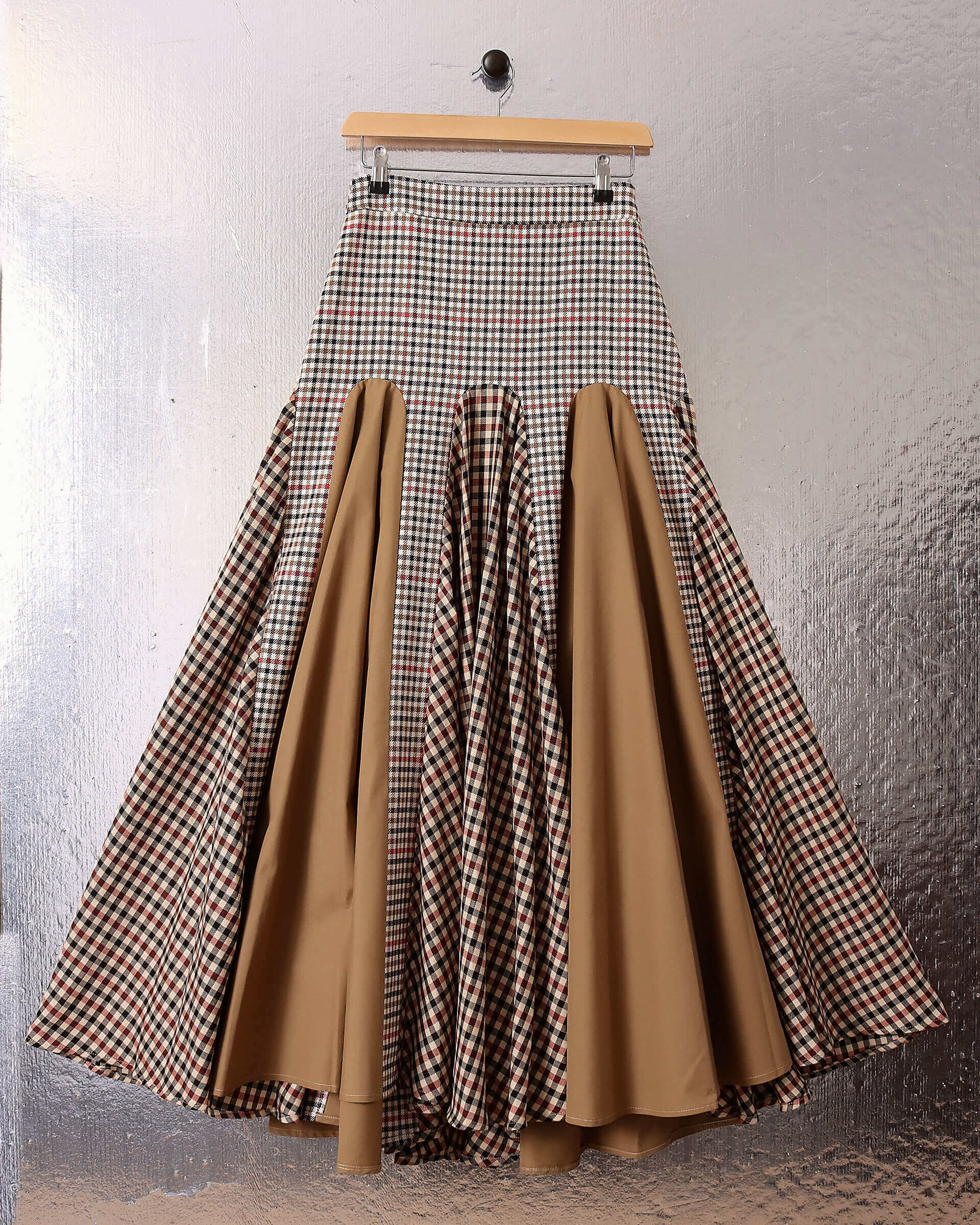 A flat shot of the 'Taali' Skirt in Check showing the alternating  eight red, black, brown, and beige check and beige poplin sections.