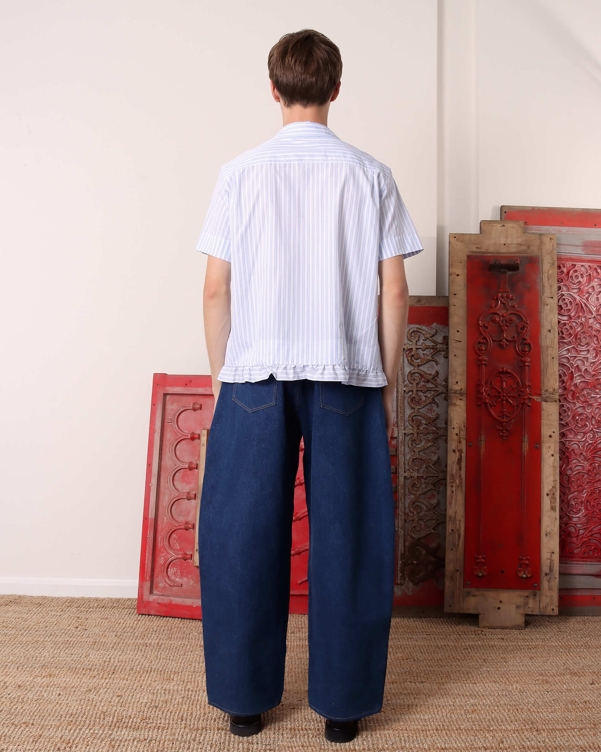 A model shows the back of the he 'Oxford' Striped Pillowcase Shirt in blue and white stripes with continued ruffles on the hem.
