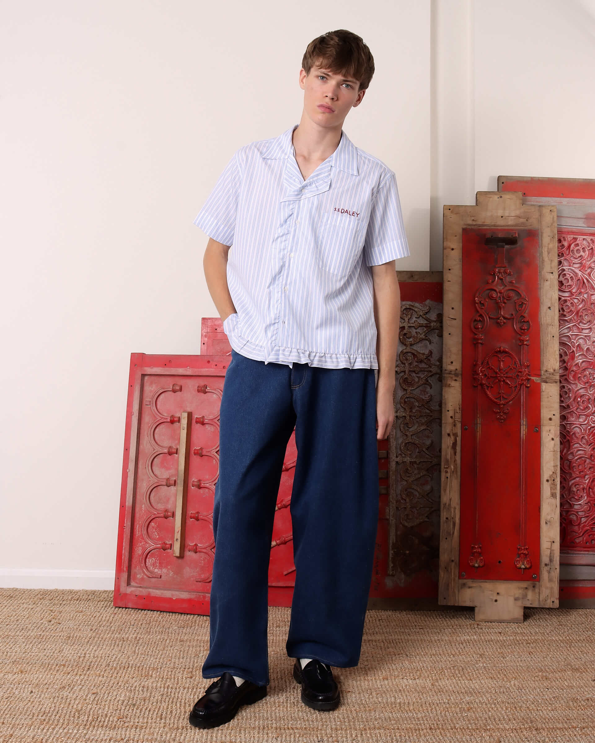 A model wears the he 'Oxford' Striped Pillowcase Shirt in blue and white stripes paired with blue denim.