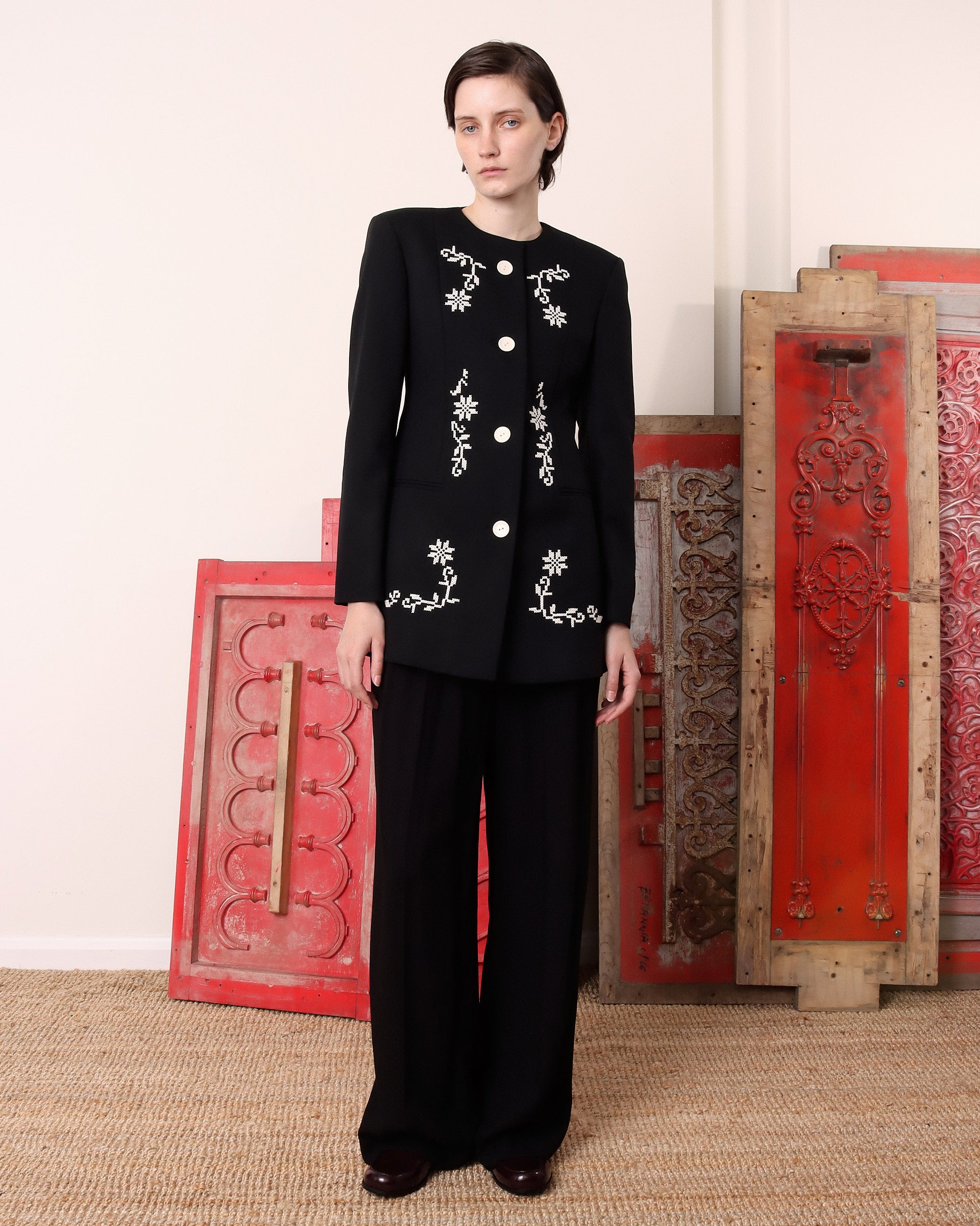 A model wears the 'Ophelia' Jacket in black with intricate white floral embroidery with it's four buttons buttoned up to the collar.