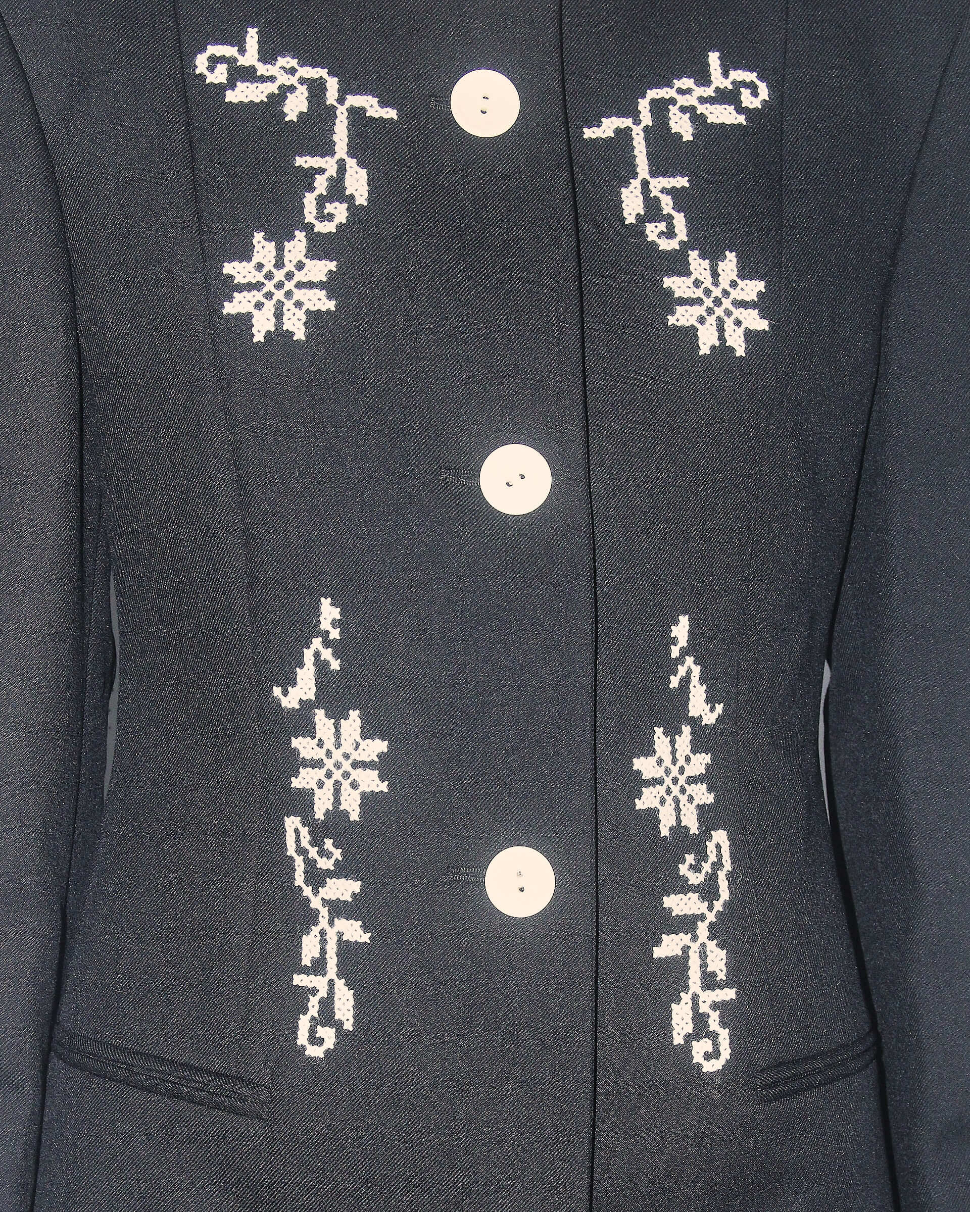 A detail shot of the 'Ophelia' Jacket showing its black tailoring wool, white decorative embroidery, and white buttons.