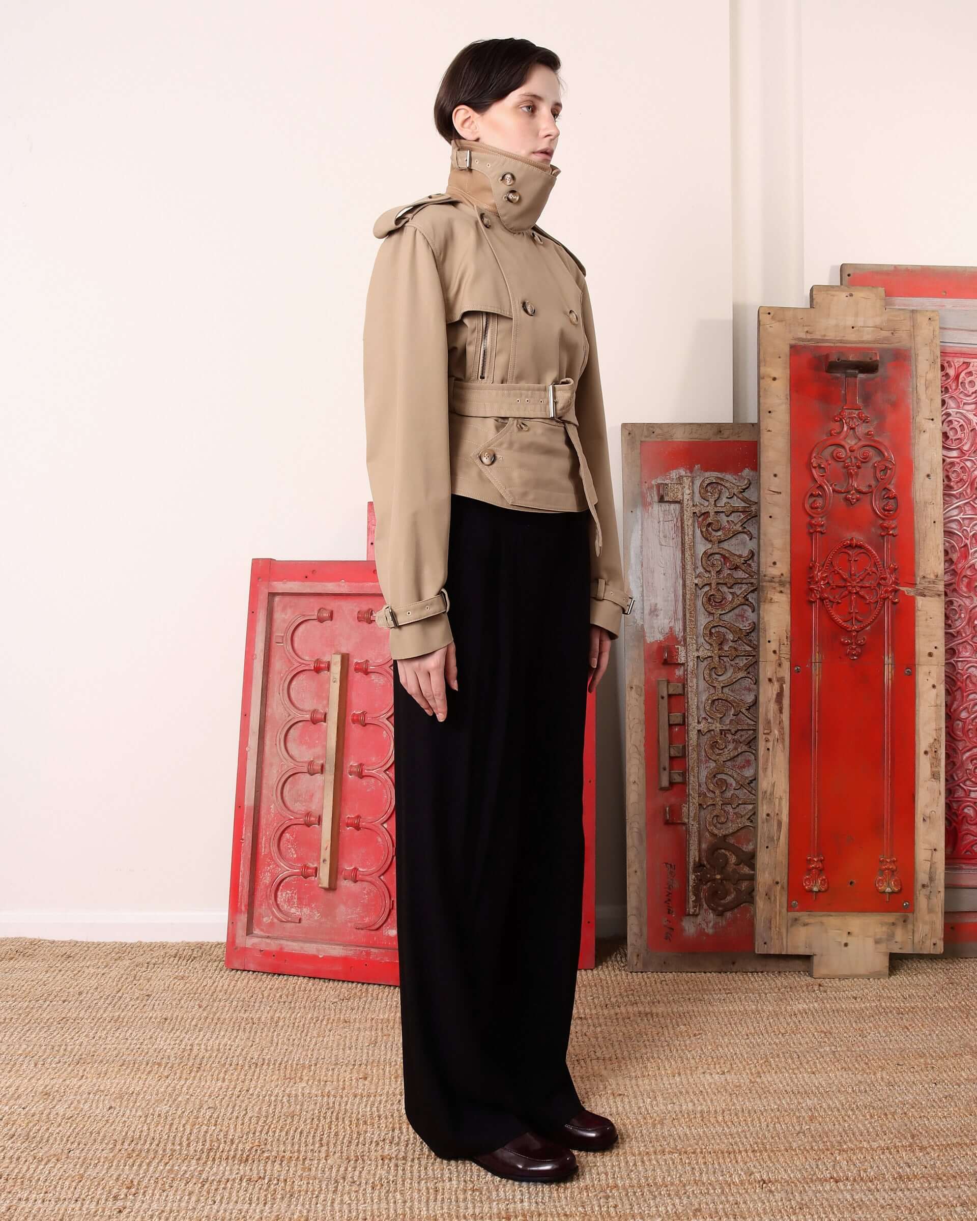 A model shows the side of the 'Eliza' Peplum Trench with the adjustable buckled neck closure fastened.