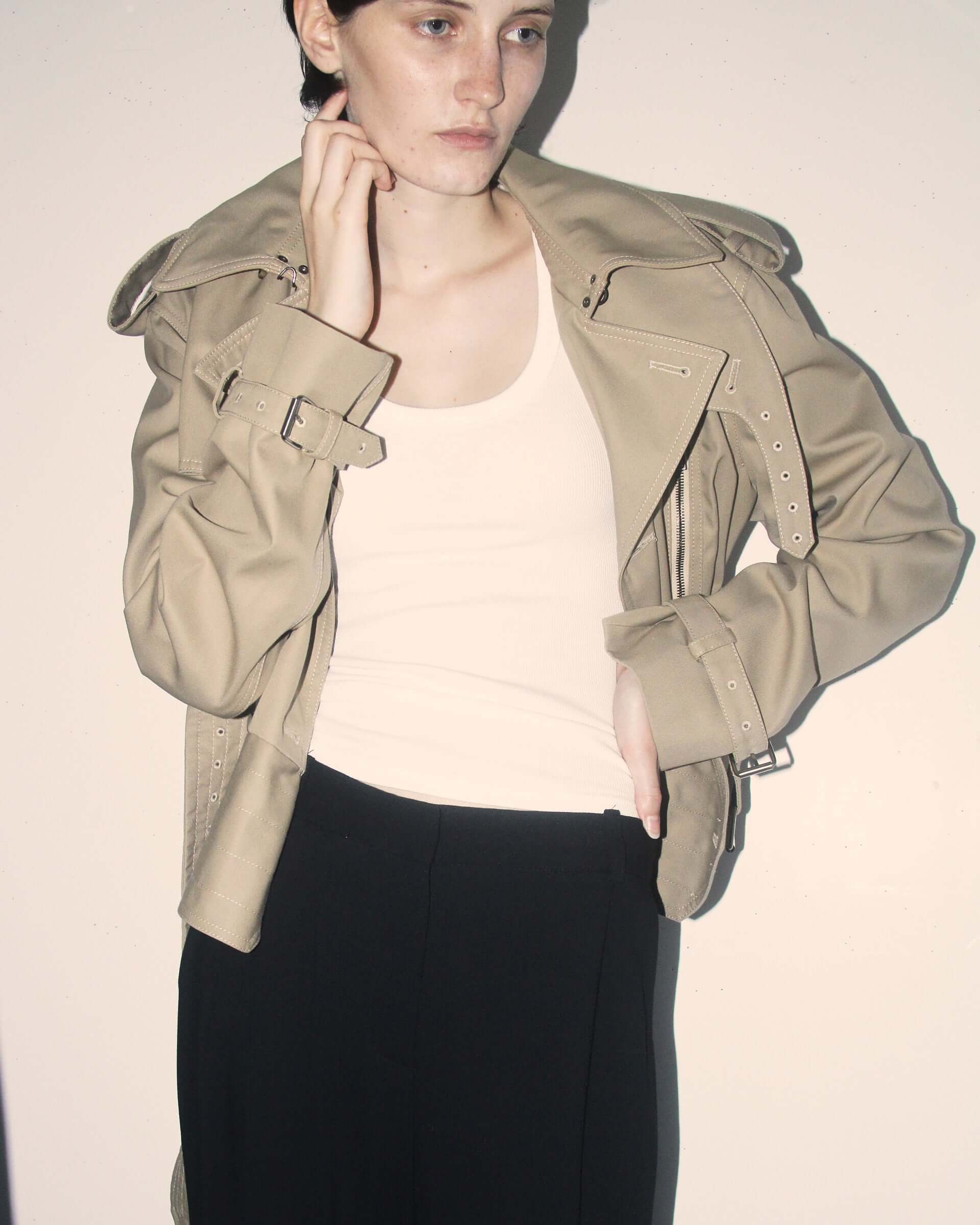 A detail shot of a model wearing the 'Eliza' Peplum Trench opened with a white vest on underneath.