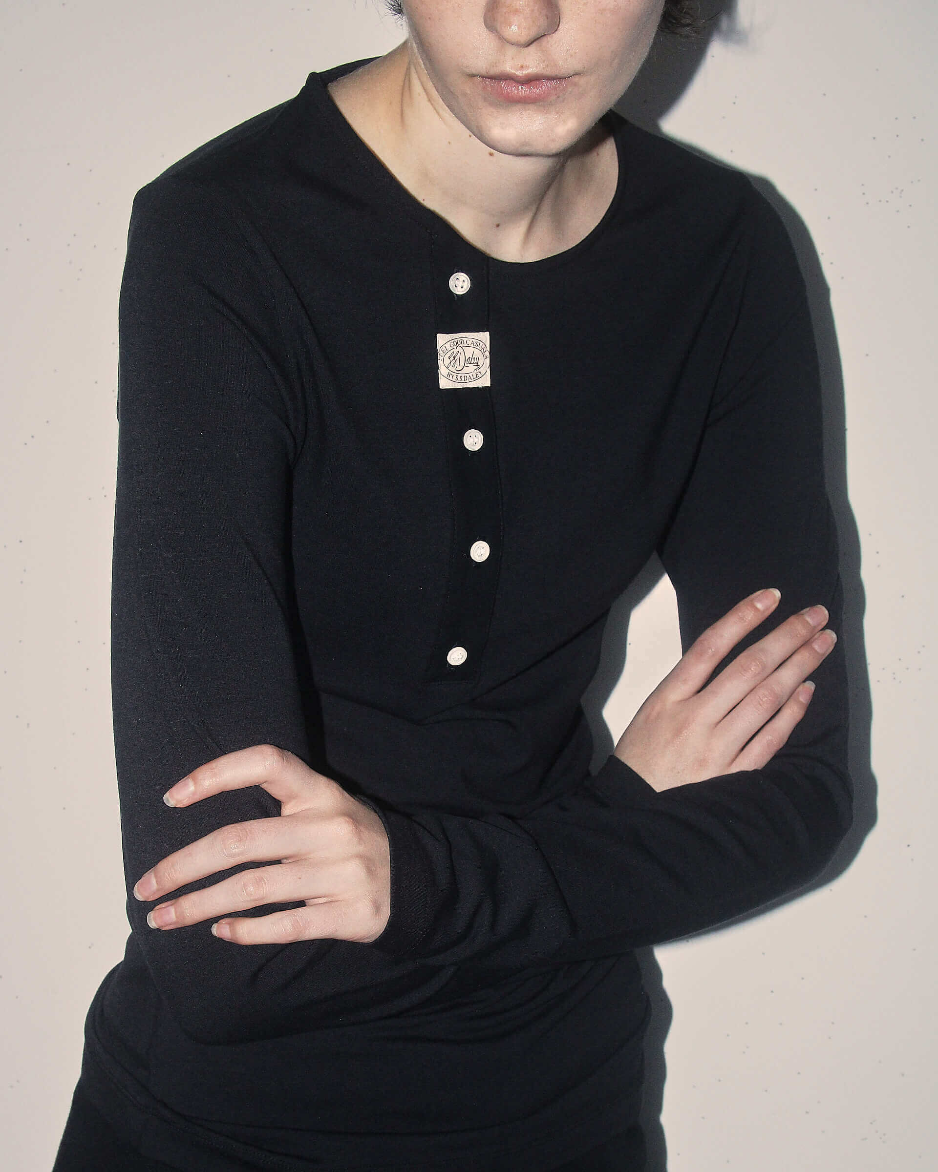 A close up of a model wearing the black 'Aker' Henley crossing her arms.