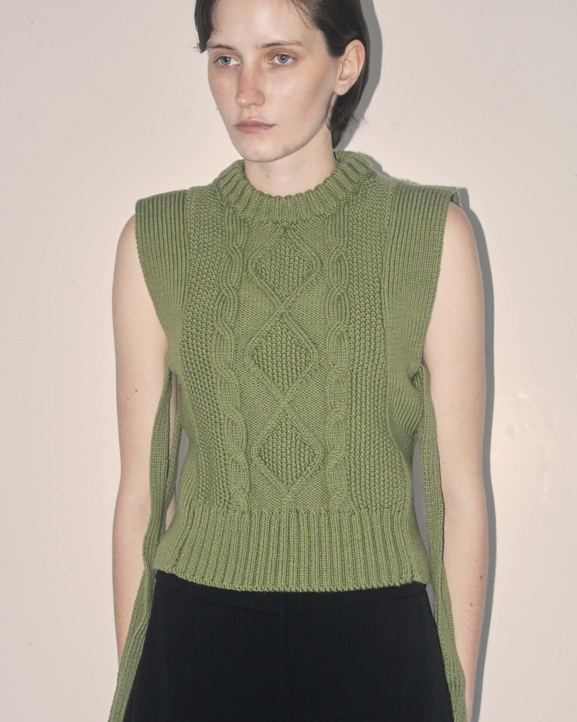 A detail shot of the cable knit pattern on the front of the green 'Blandine' Vest on a model with the side-ties untied.
