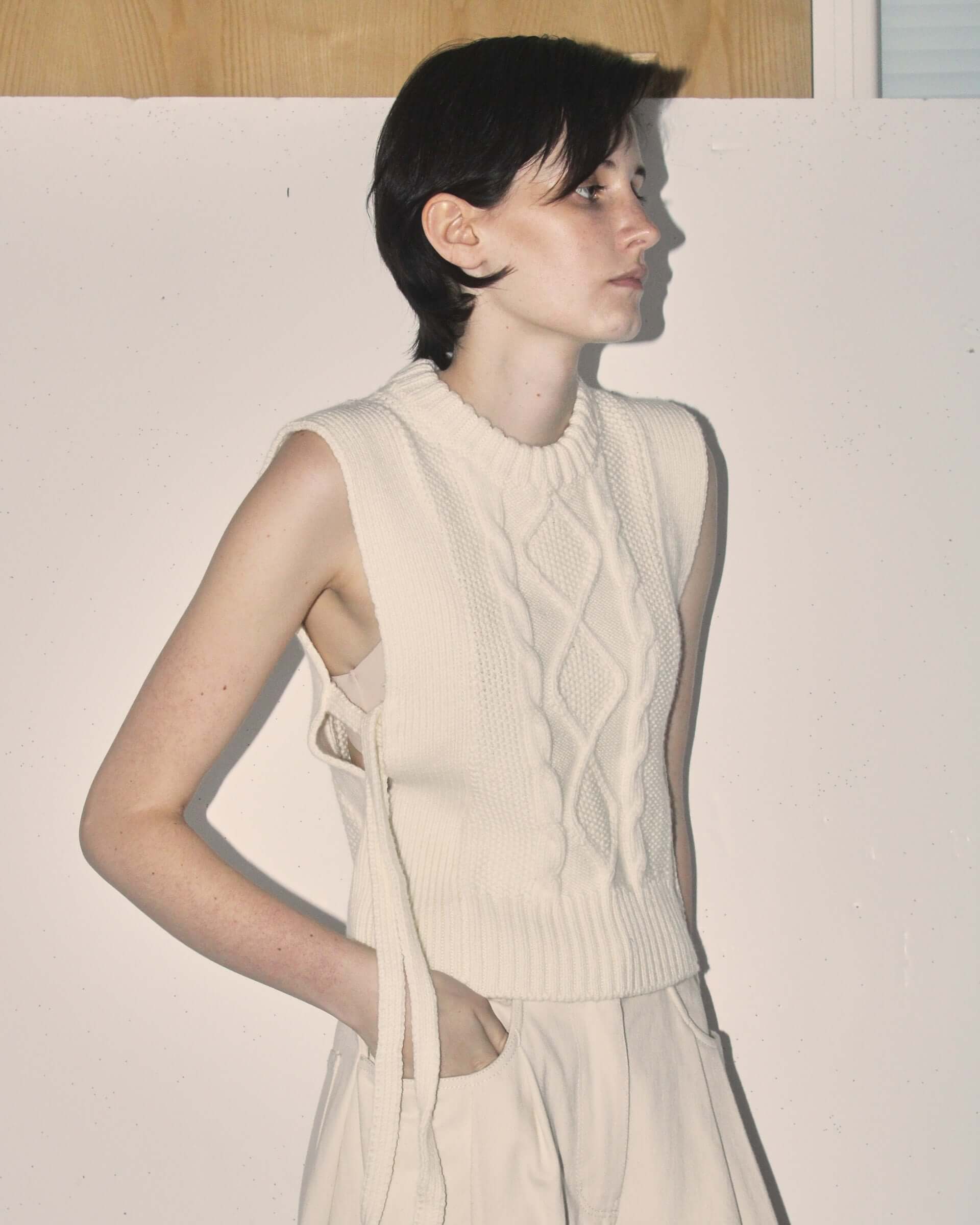 A detail shot of a model wearing the ecru 'Blandine' vest with the side-tie details untied.