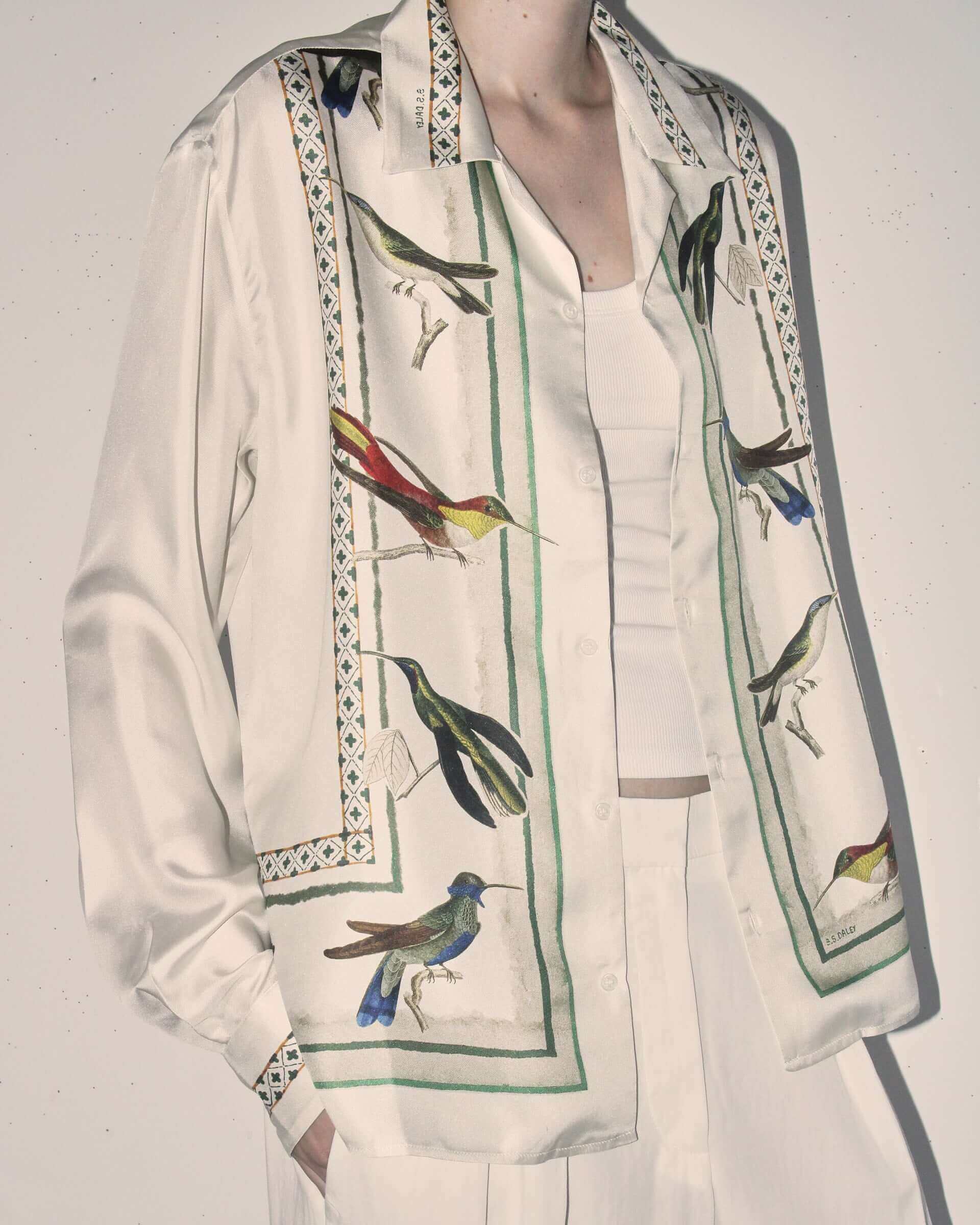 A close up of the print on the silk shirt on a model, showing the realistic hummingbirds in detail as well as the weave and line patterns running along the shirt and a hidden green S.S.DALEY text on the collar.