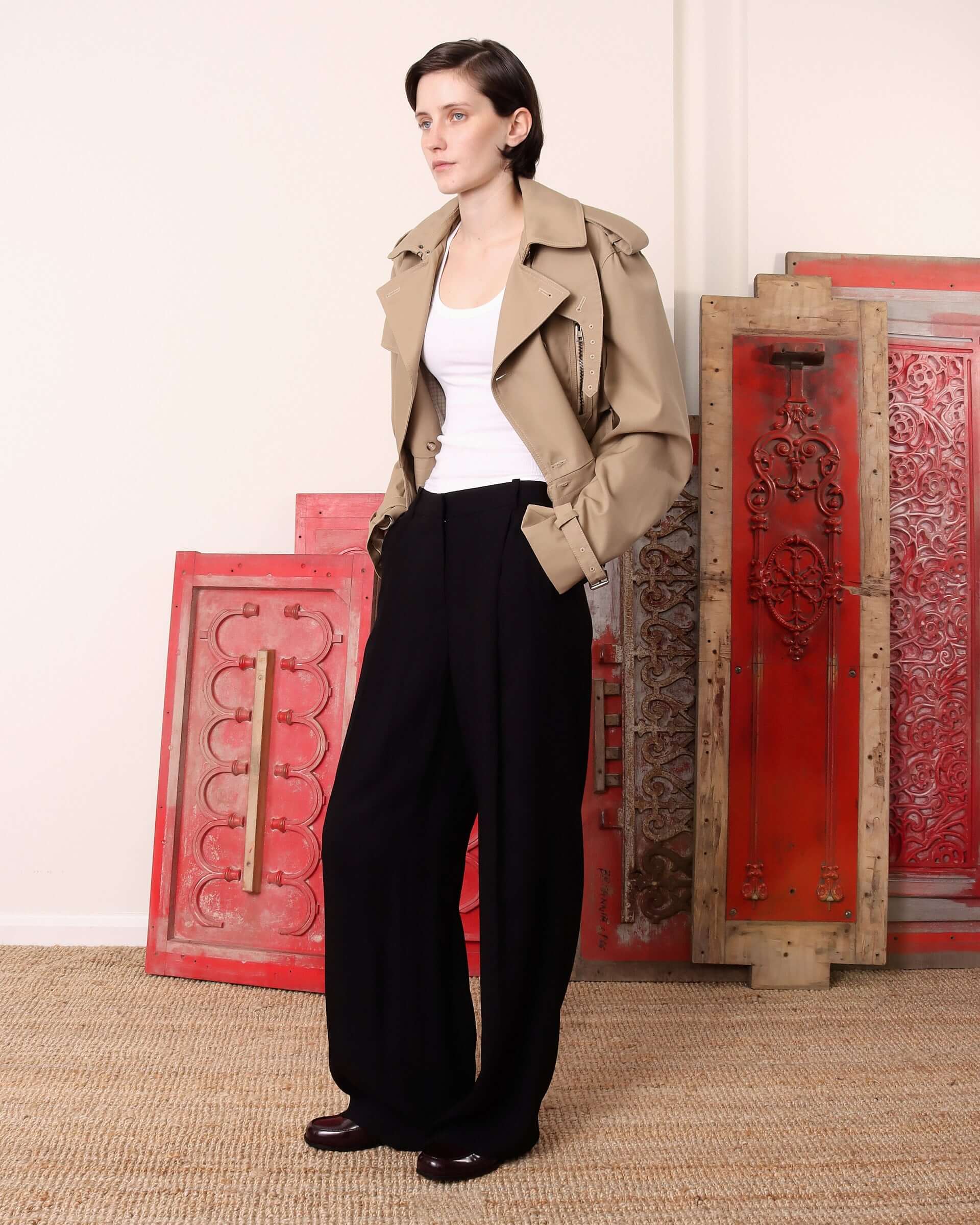 A model wears the 'Eliza' Peplum Trench open with her hands in the pockets of the black trousers she's been styled with.