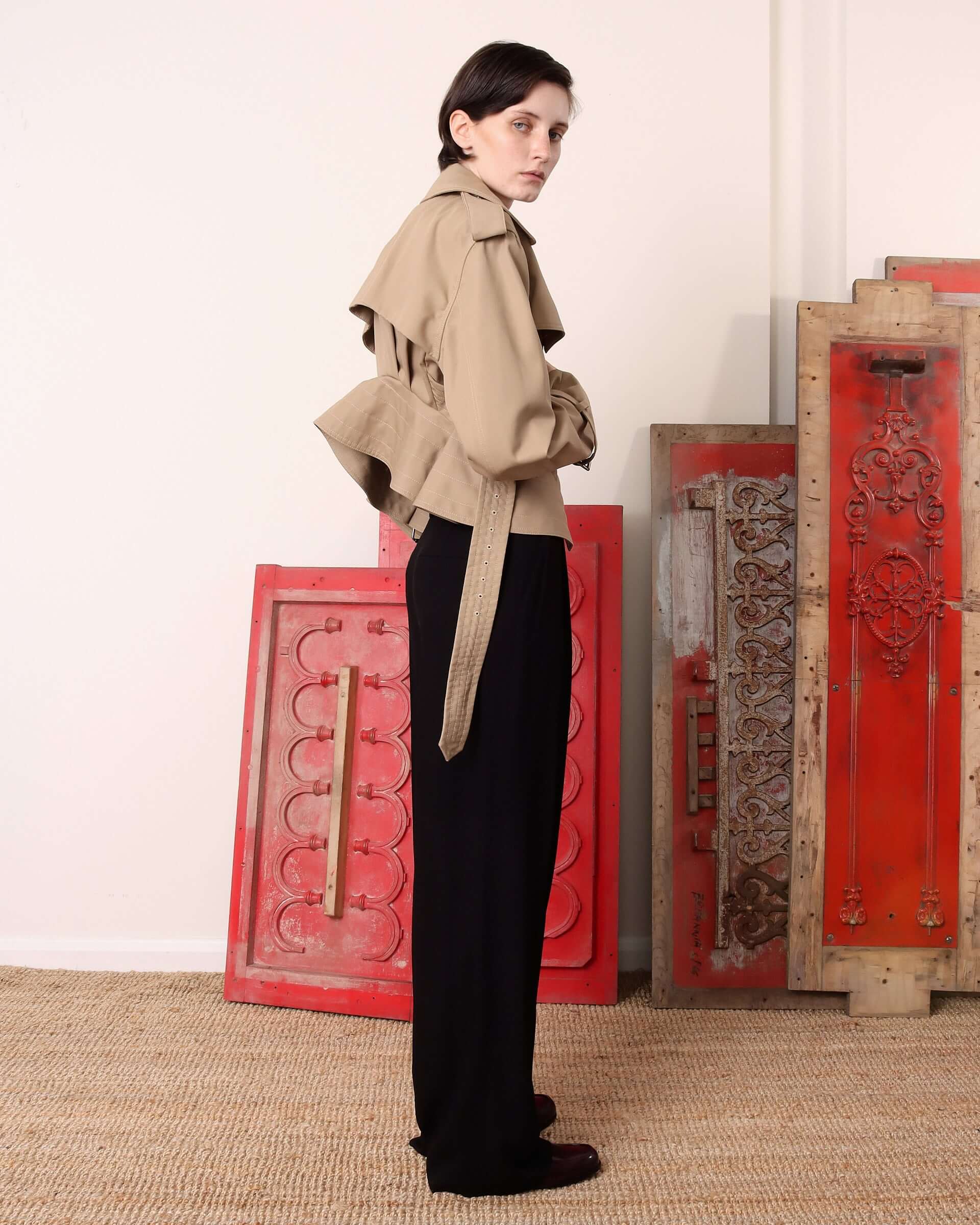 A model shows the side of the 'Eliza' Peplum Trench and the way the cinched waist flares into a pleated peplum silhouette.