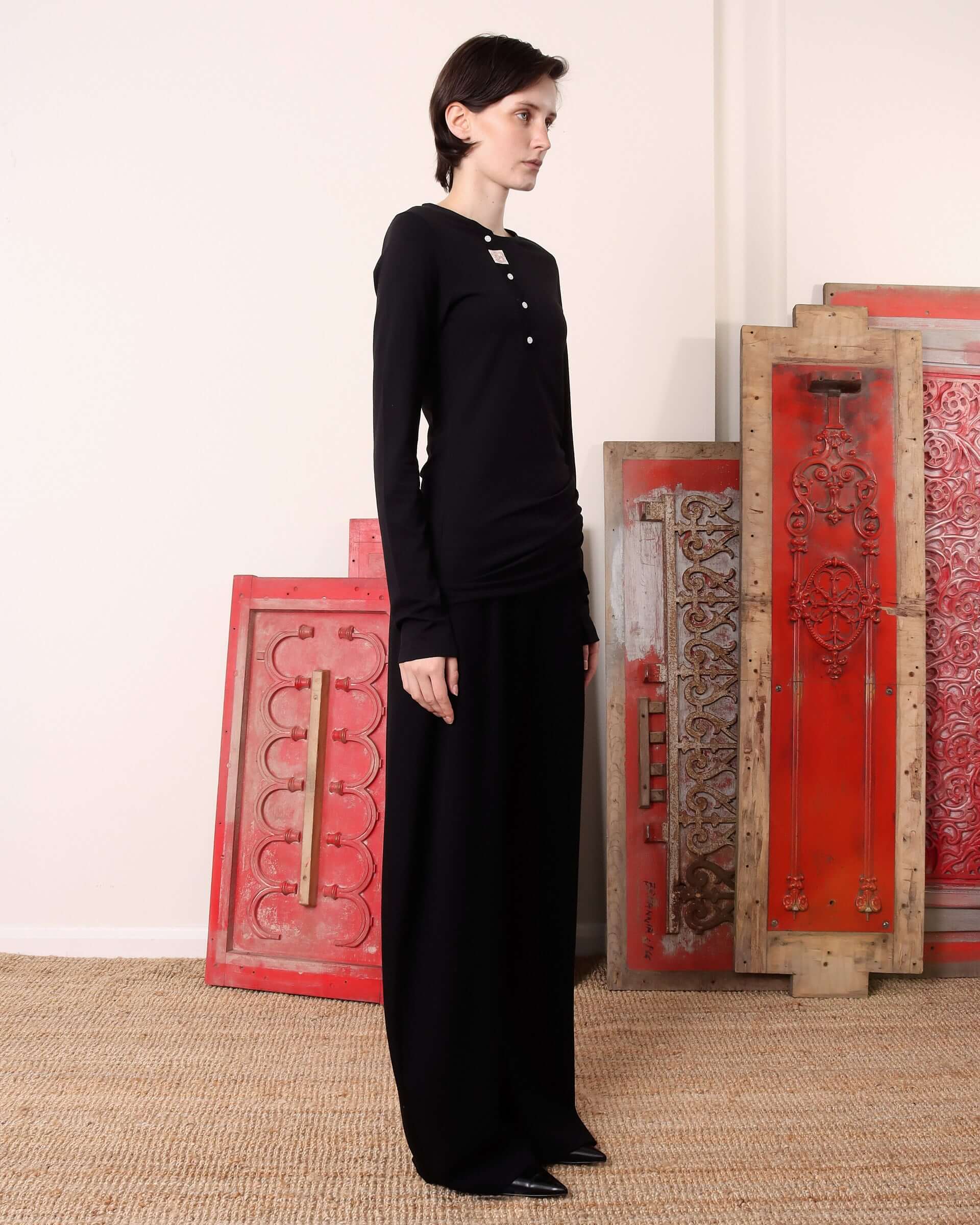 A model shows he side of the long sleeve 'Aker' Henley in black.