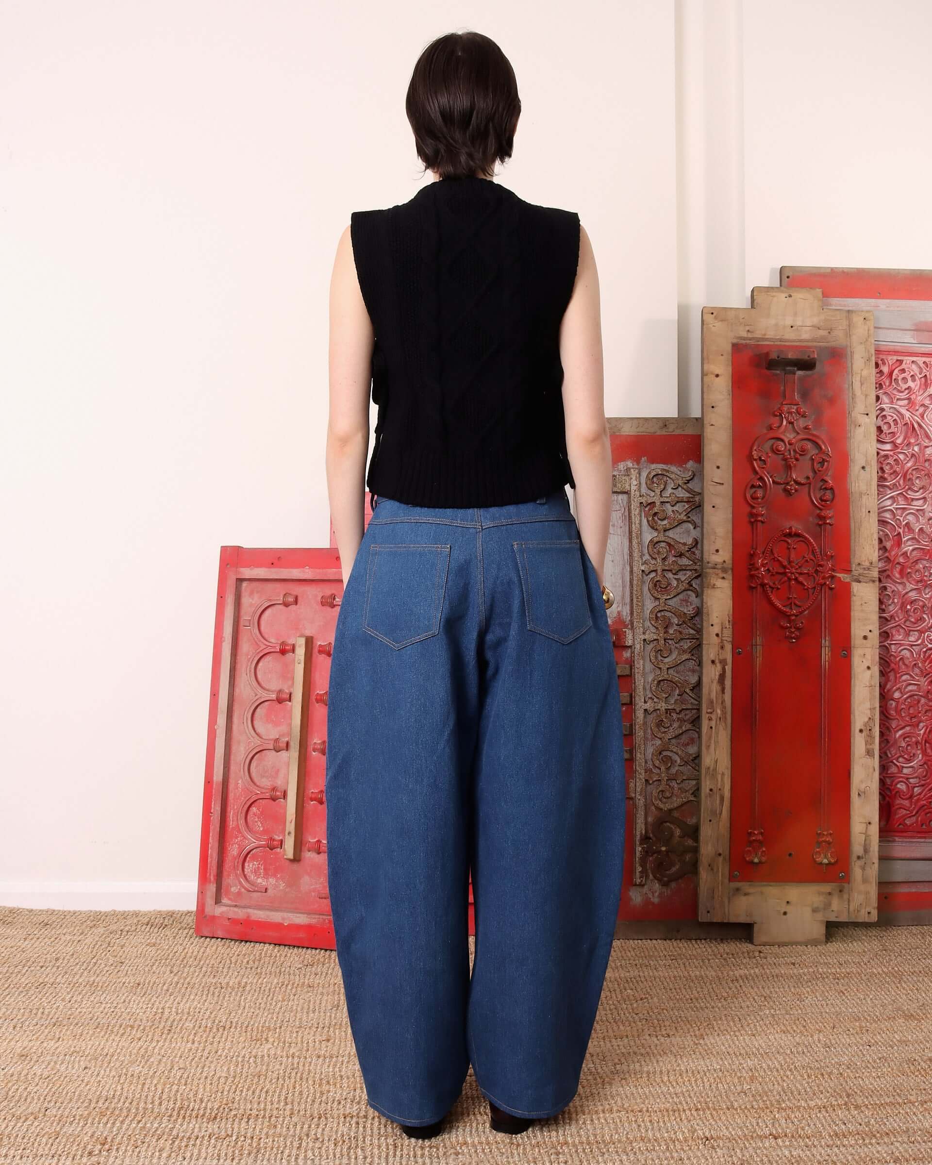 A model shows the back of the black 'Blandine' Vest and the paired blue denim trousers.