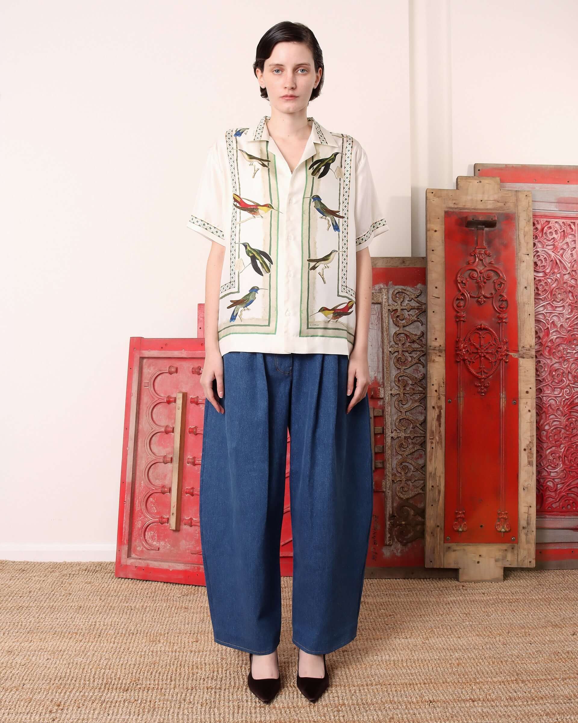 A model wears the short sleeved 'Birdwatcher' shirt with pleated denim jeans for a completed look.