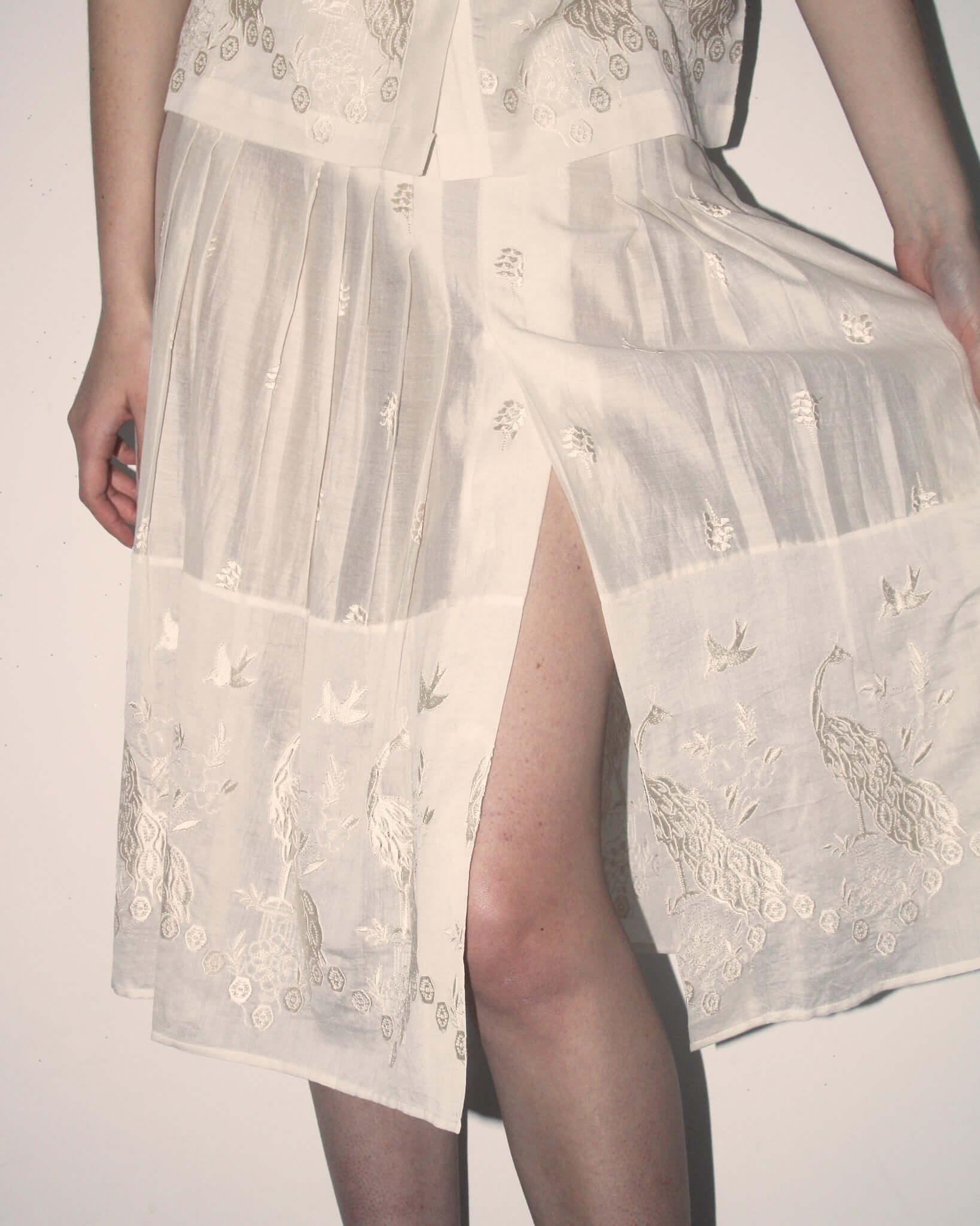 A detailed shot of the 'Ada' Skirt in white showing the split hem and subtle bird and peacock motifs.